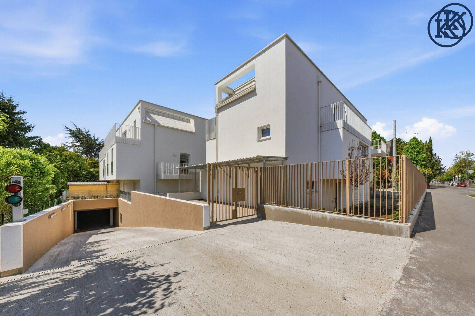 Außenansicht des modernen Wohnkomplexes mit Zufahrt zur Tiefgarage und umzäuntem Grundstück.