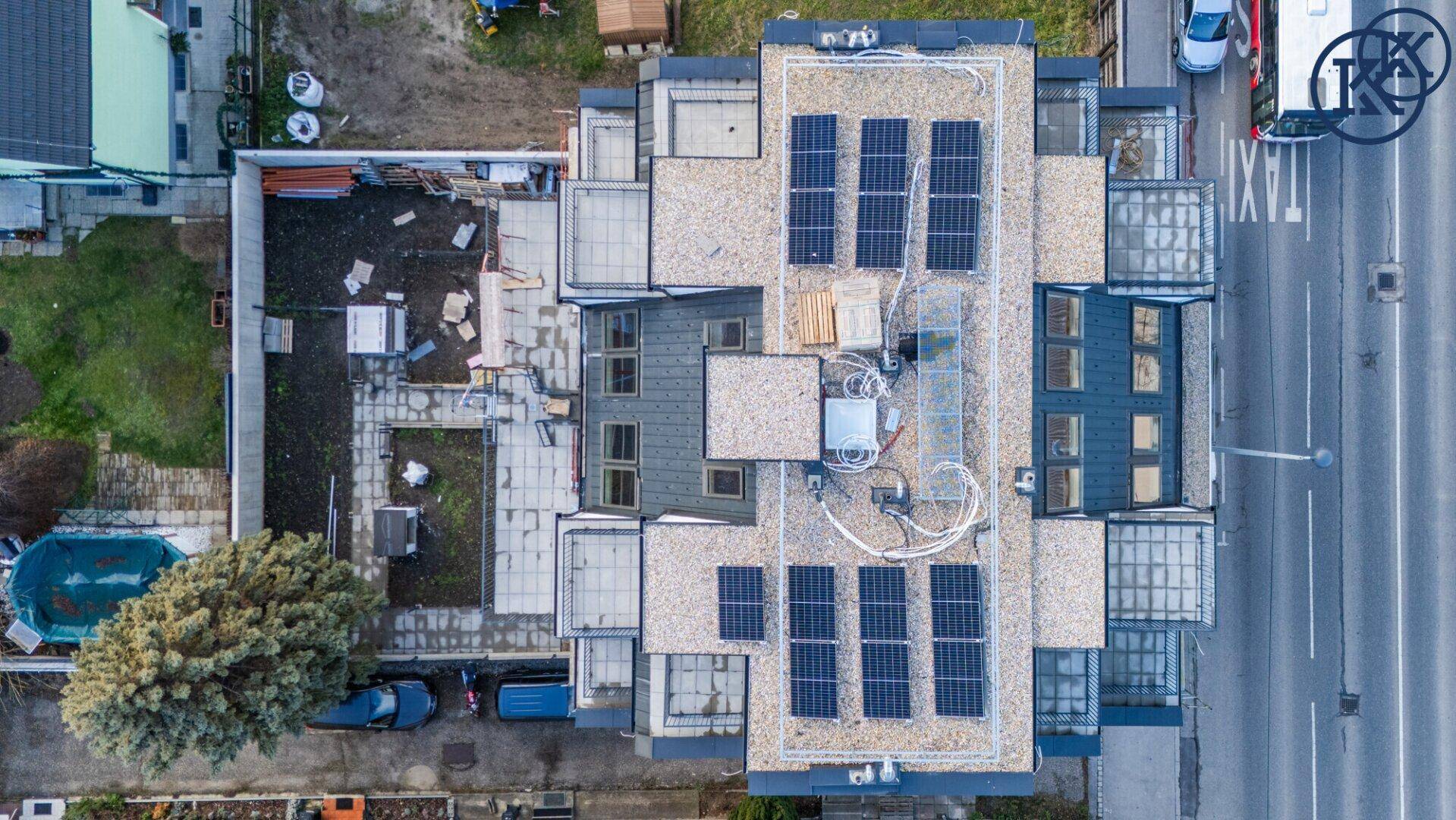 Luftaufnahme des modernen Wohngebäudes mit Solaranlagen auf dem Dach und umliegenden Gärten.