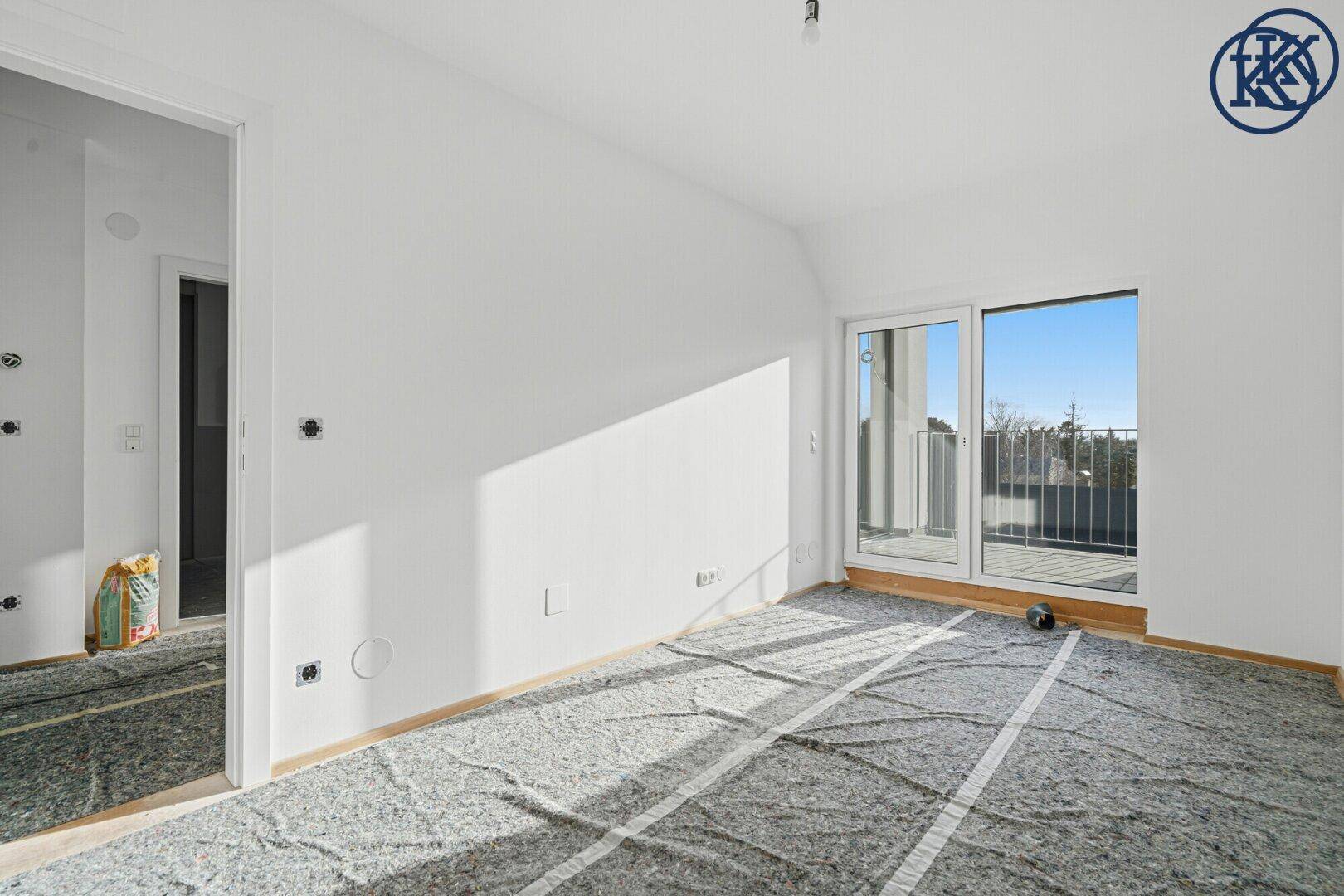 Geräumiges Zimmer im Bau mit weiß gestrichenen Wänden und Balkonzugang.