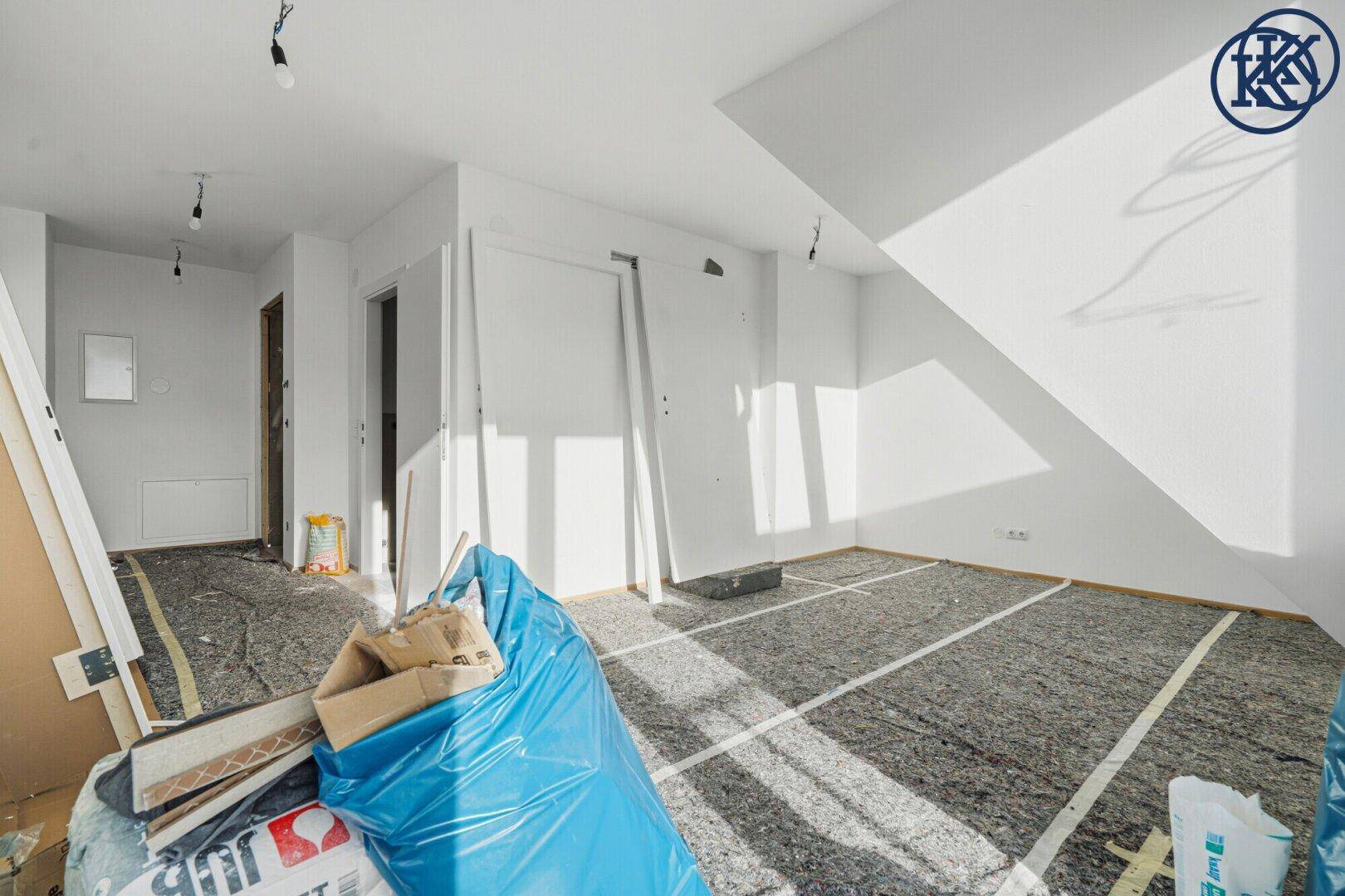 Geräumiges Dachgeschosszimmer im Bau mit schrägen Wänden und Baumaterialien.