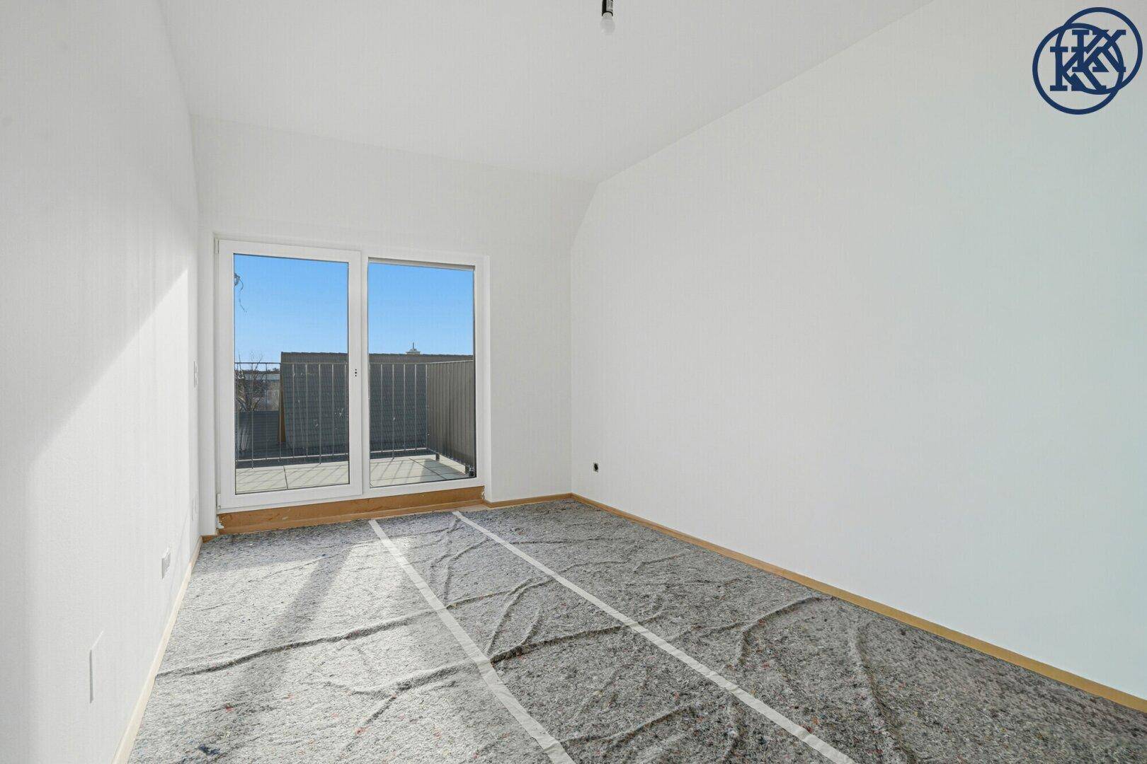 Helles Schlafzimmer im Rohbau mit Zugang zu einem Balkon und viel Tageslicht.