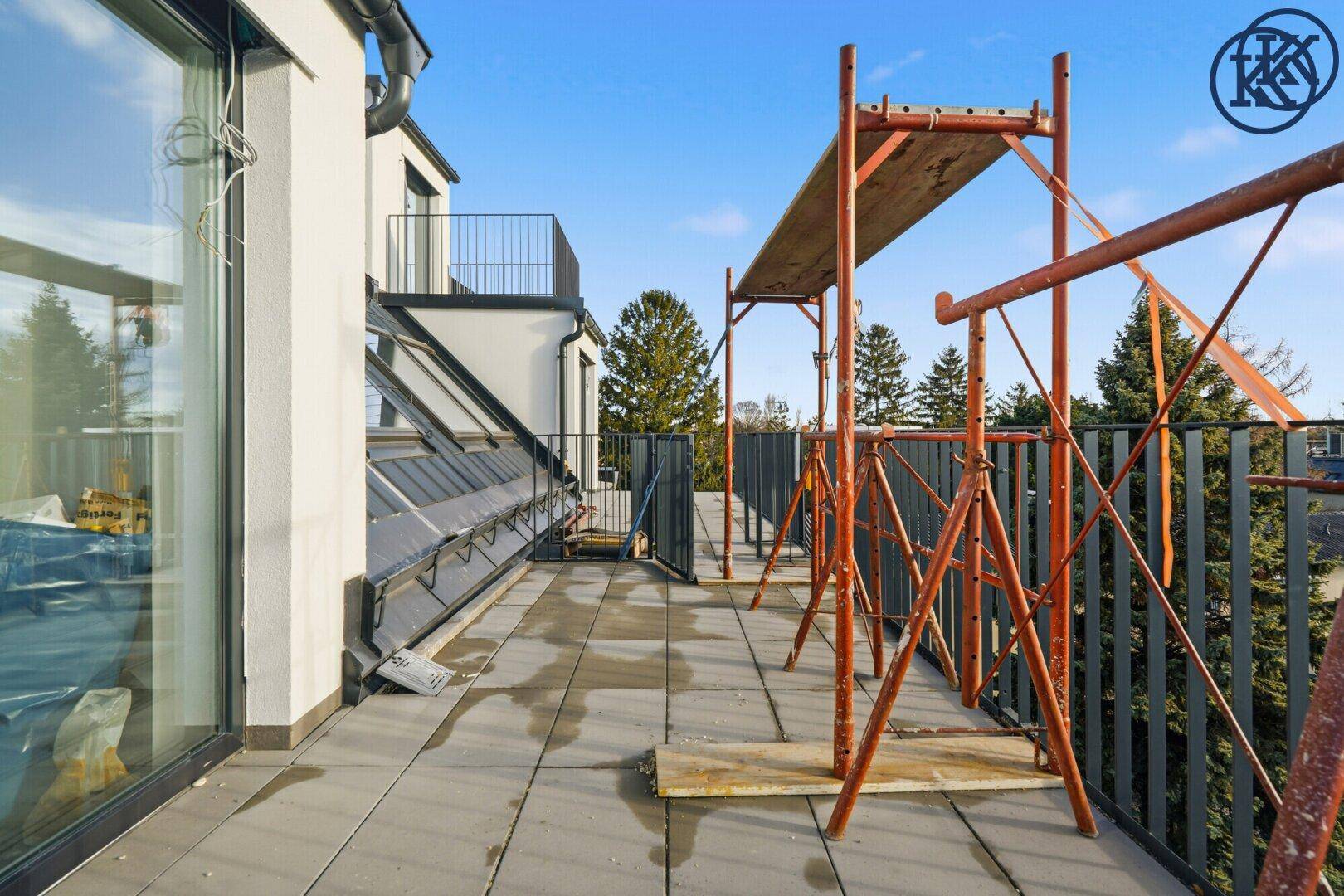 Weitläufige Terrasse im Bau mit Gerüst und Blick auf Bäume und Häuser.