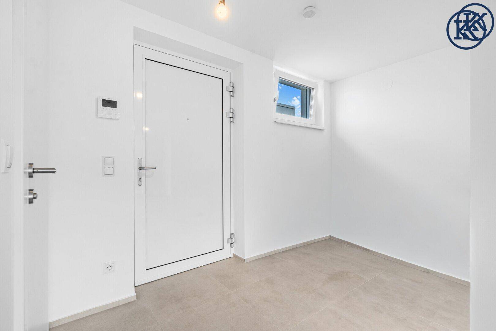 Heller Eingangsbereich mit weißer Tür, Fliesenboden und kleinem Fenster.