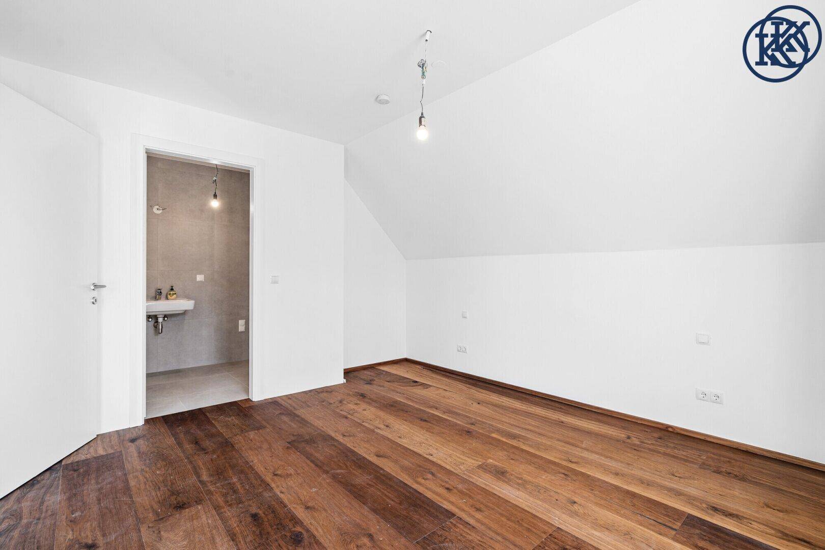 Schlafzimmer mit Holzboden und direktem Zugang zu einem modernen Badezimmer.