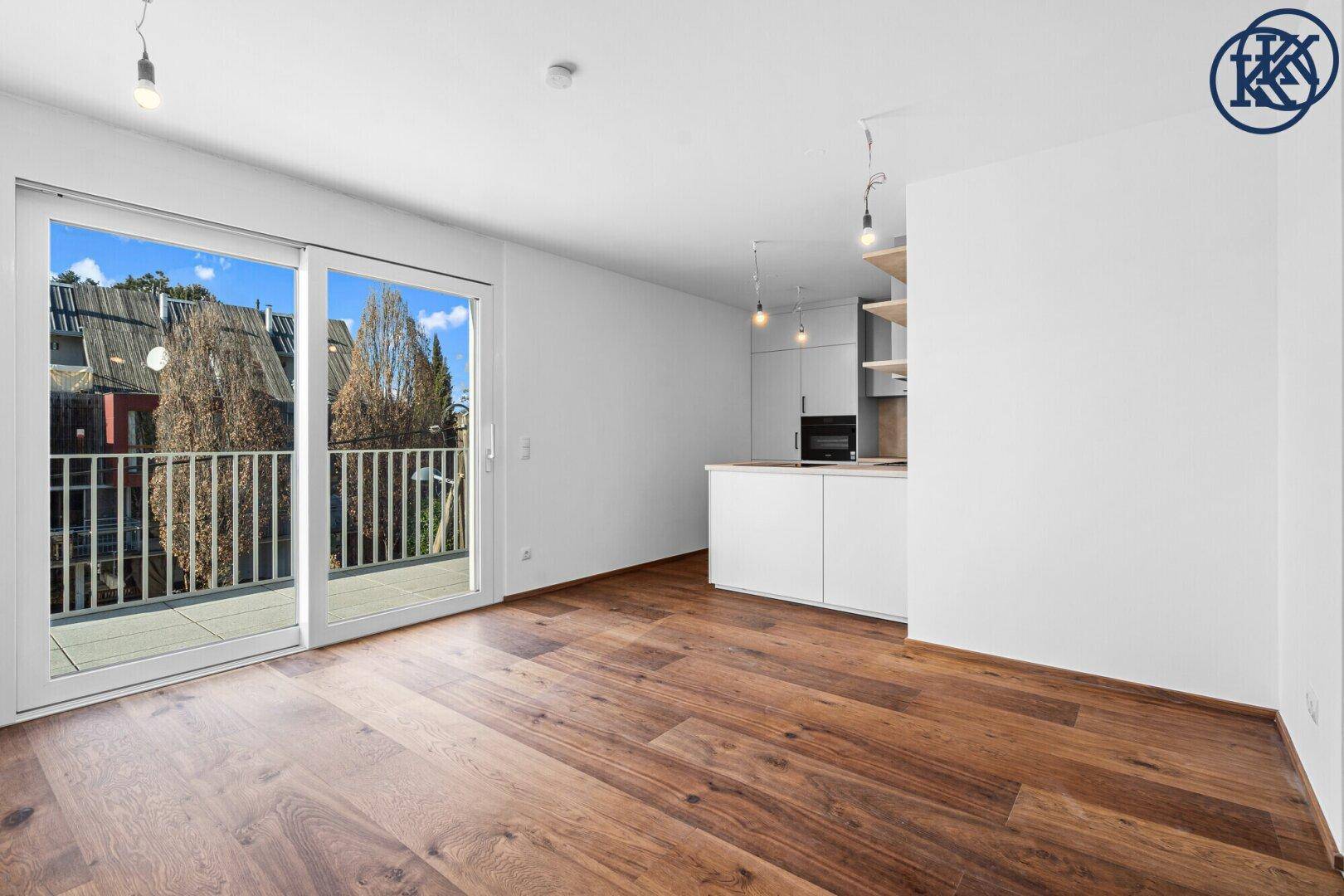 Heller Wohnbereich mit offener Küche, Holzboden und Zugang zu einem Balkon.