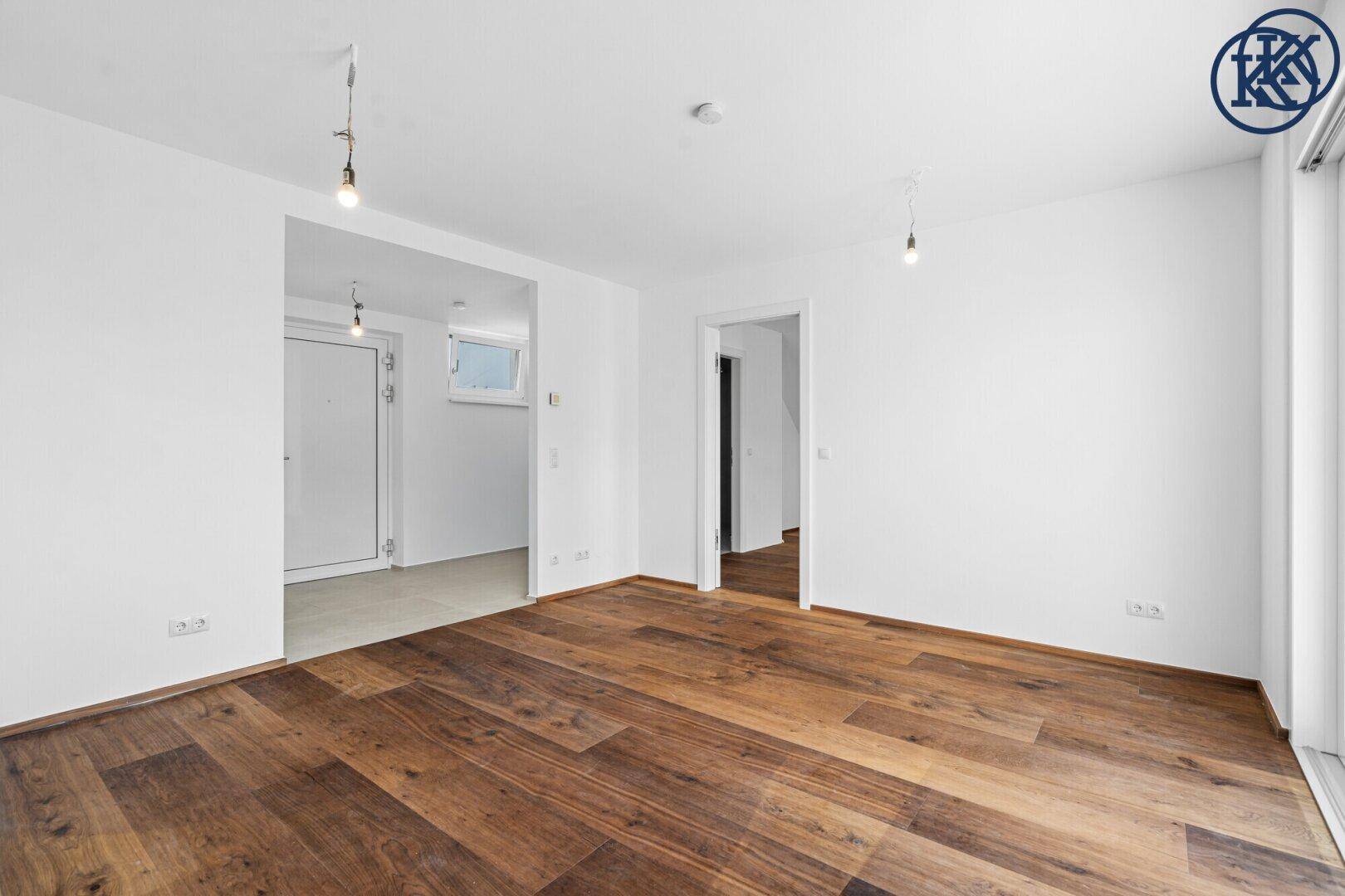 Geräumiger, heller Raum mit Holzboden und Zugang zu weiteren Zimmern.