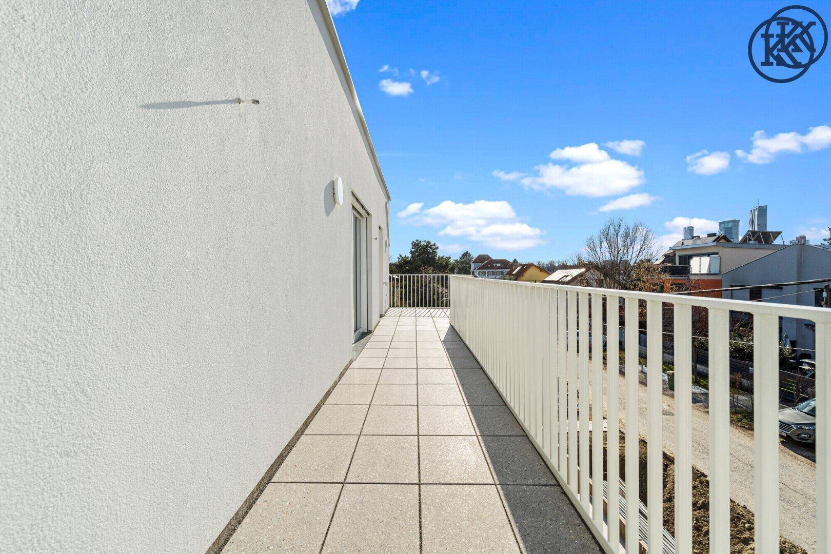 Langer, schmaler Balkon mit Fliesenboden und weißem Geländer unter blauem Himmel.
