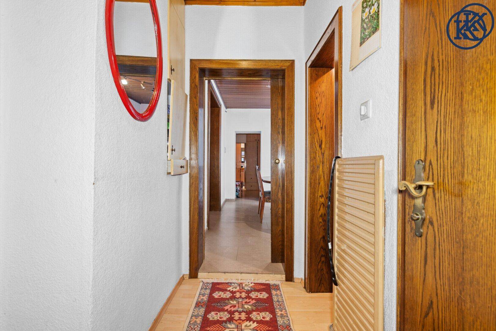 Heller Flur mit Holztüren, Holzdecke und einem Teppich auf dem Laminatboden.
