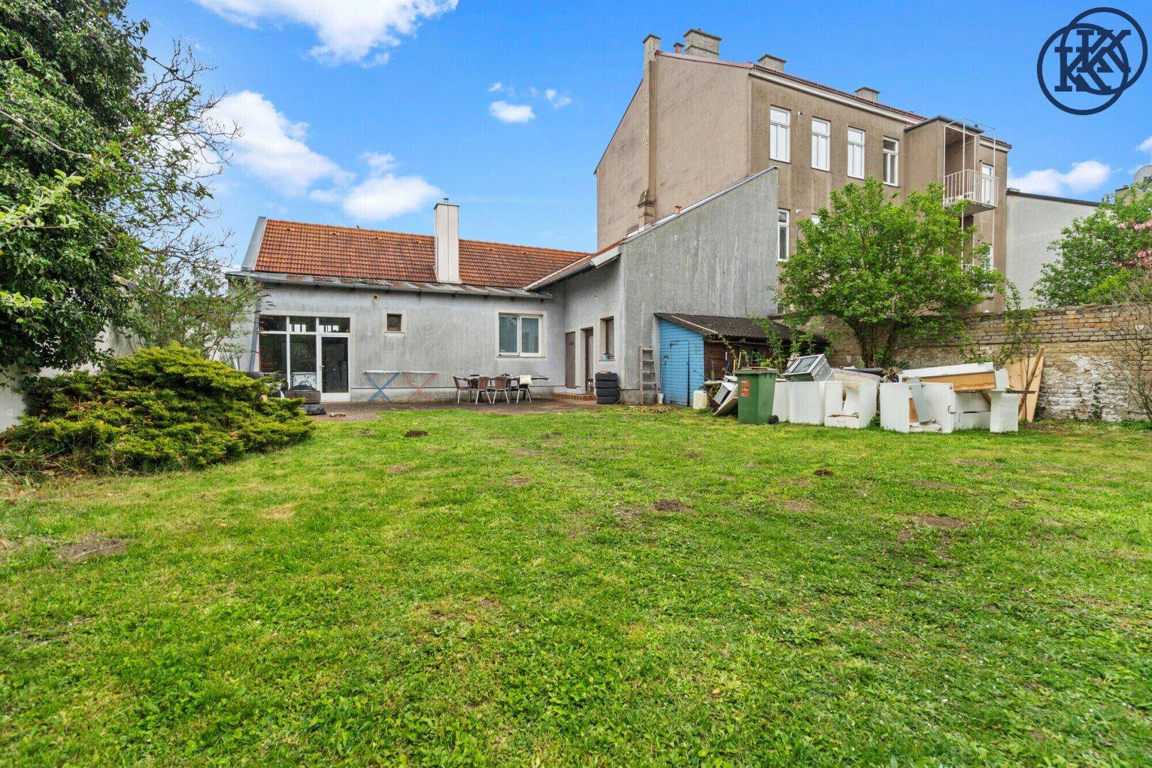 Rückansicht des Hauses mit Terrasse und großem Garten, umgeben von Bäumen.