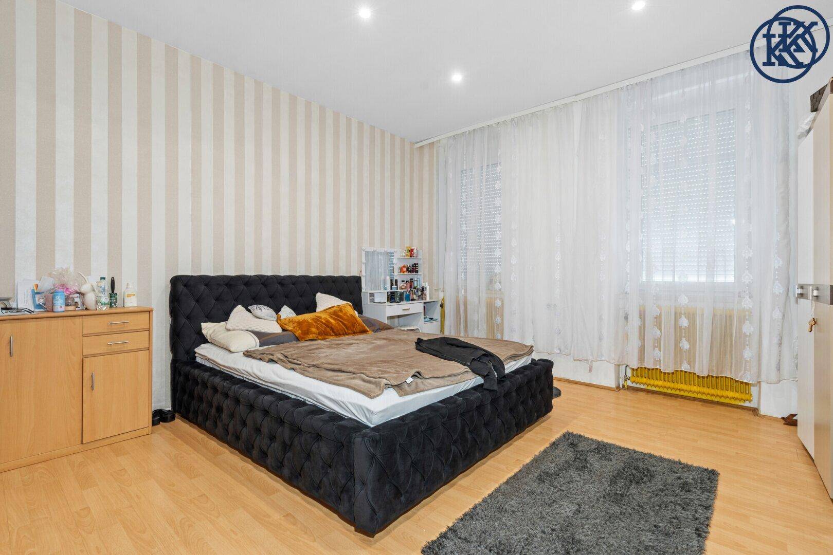 Schlafzimmer mit großem Bett, gestreifter Tapete und hellem Laminatboden.