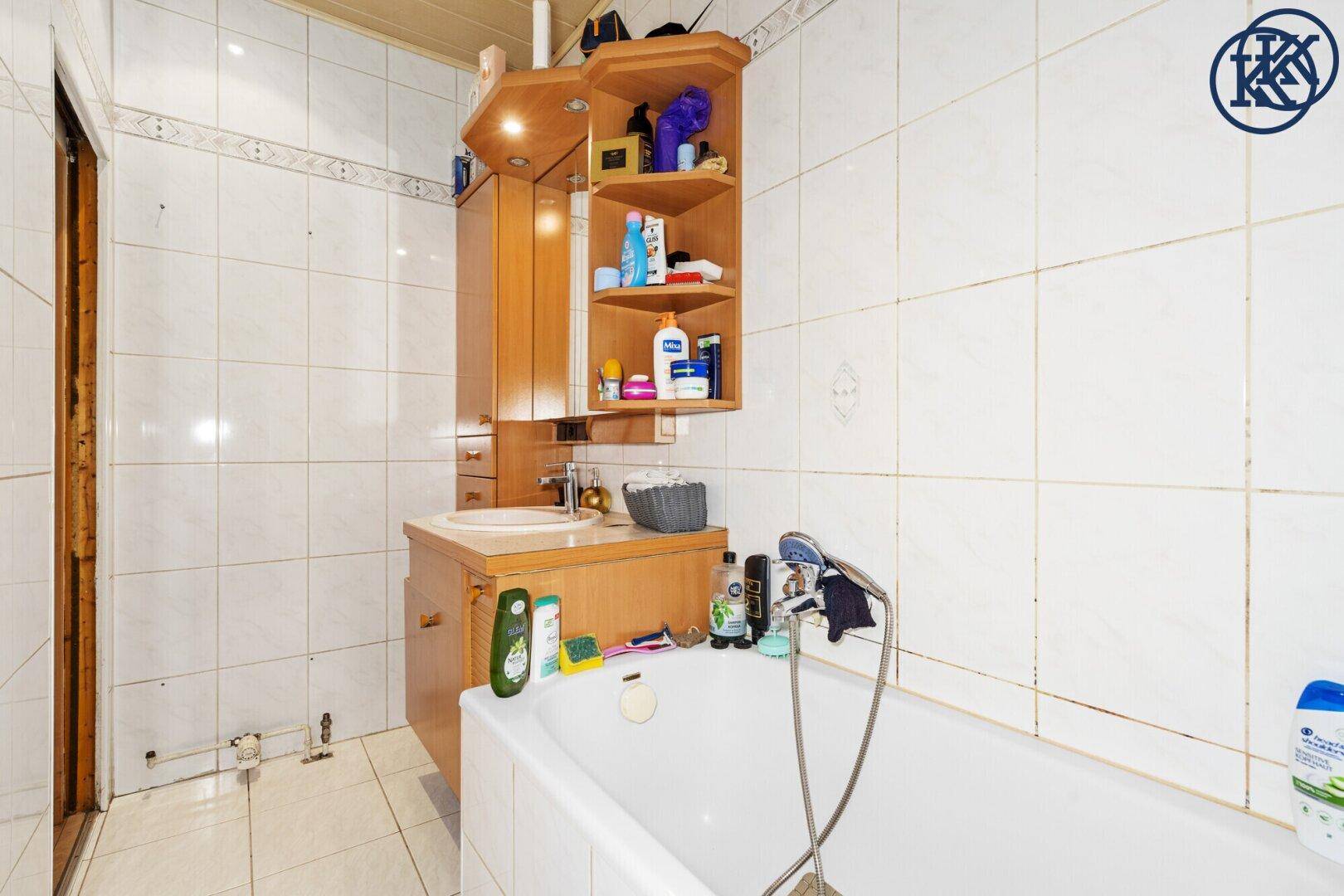 Badezimmer mit Badewanne, Waschbecken und Spiegelschrank, komplett gefliest.