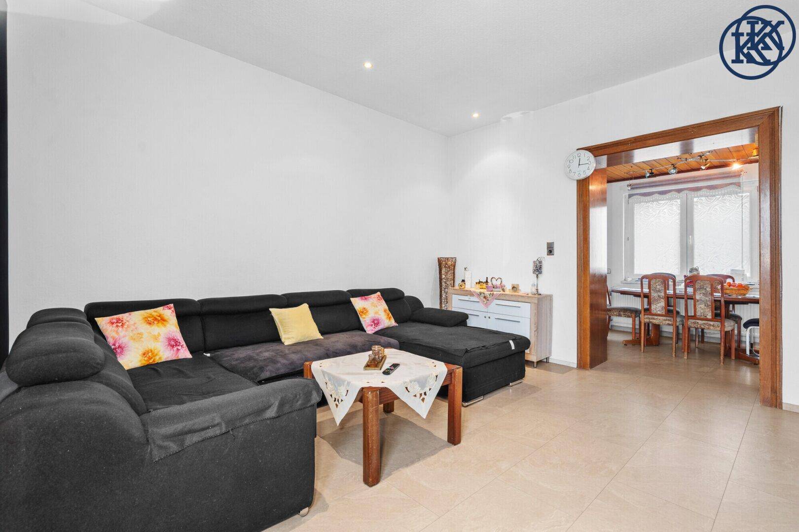Offener Wohnbereich mit Sofa und Durchgang zum Esszimmer, Fliesenboden.