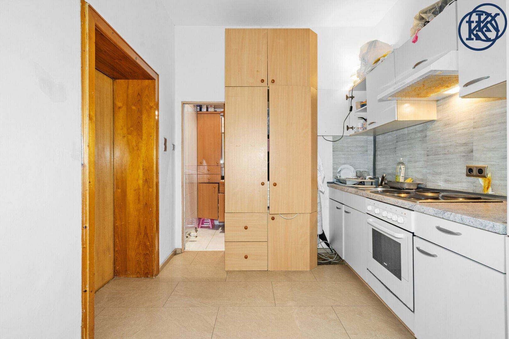 Küche mit weißen Unterschränken, Herd und einem hohen Holzschrank.