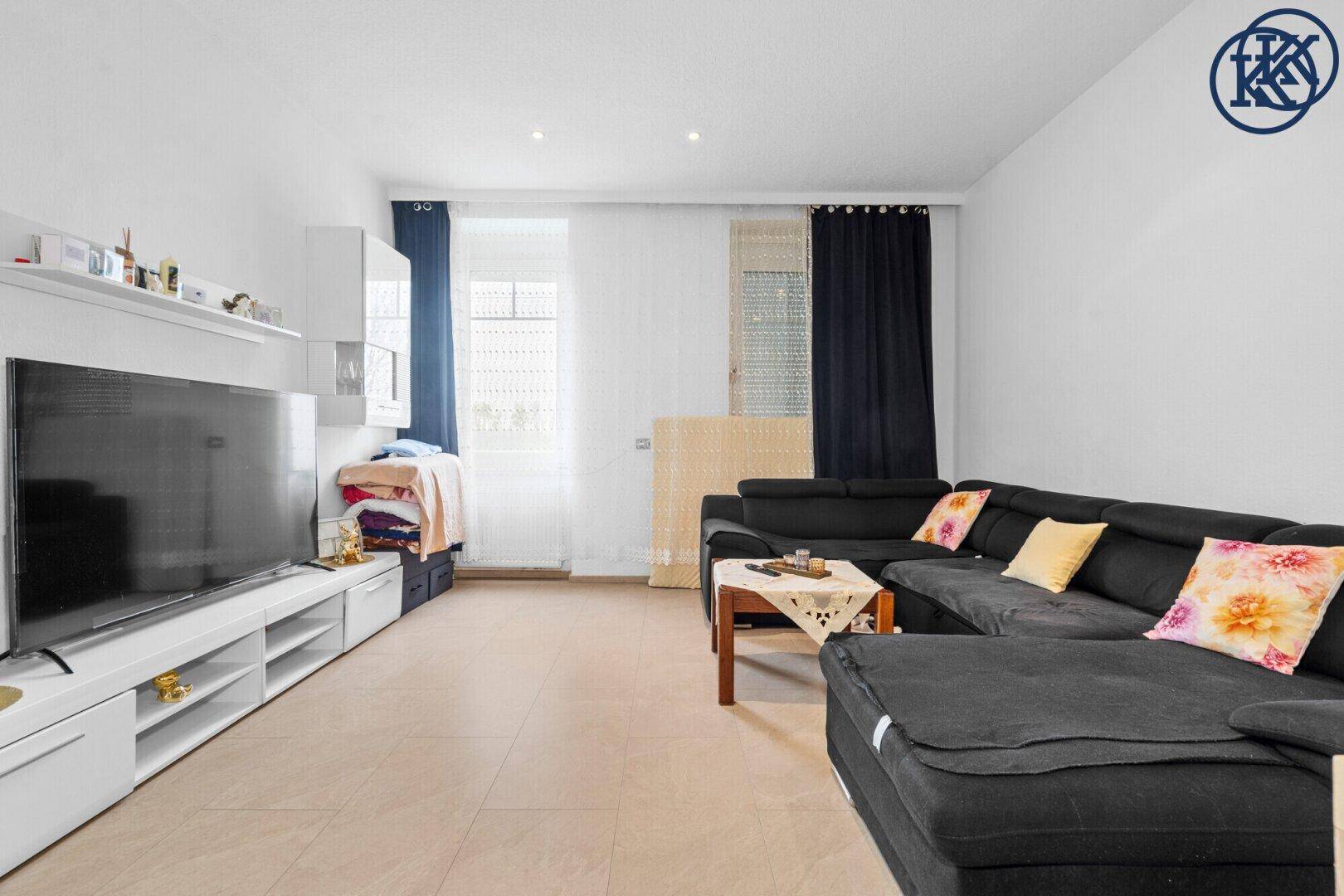 Geräumiges Wohnzimmer mit großem Sofa, Fernsehmöbel und Fliesenboden.