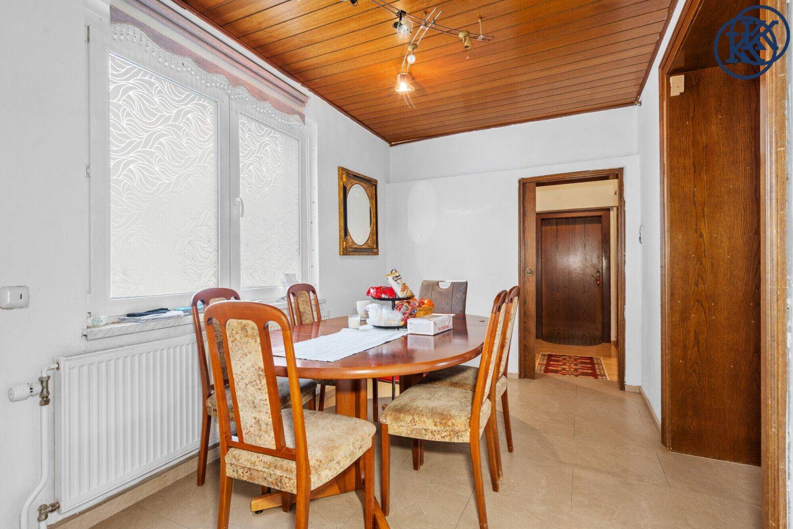 Essbereich mit Holztisch, Stühlen und einem Fenster, das Tageslicht hereinlässt.