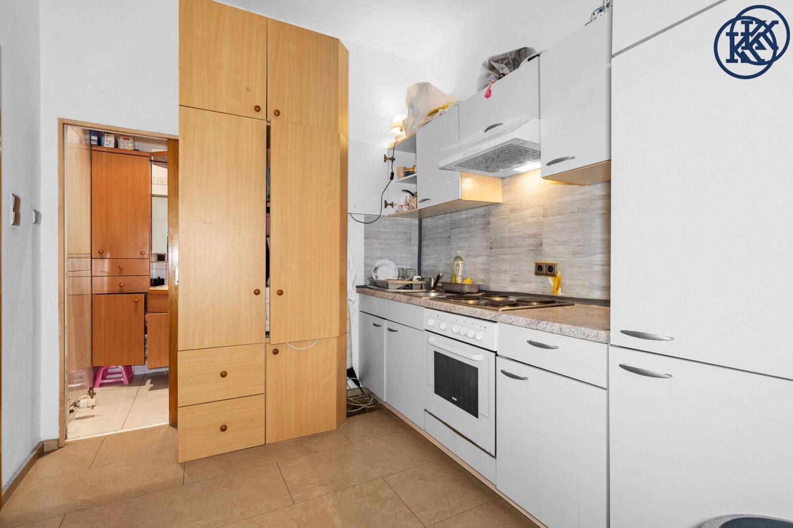 Funktionale Küche mit weißen Schränken, Fliesenboden und Holzschränken.