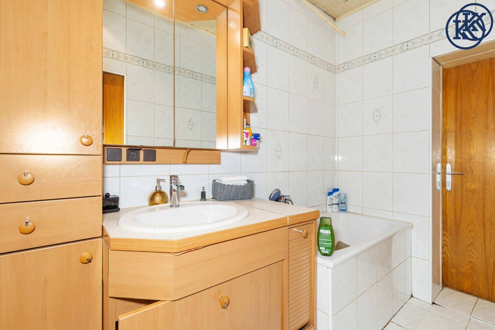 Badezimmer mit Badewanne, Waschbecken und Holzschränken, gefliesten Wänden.