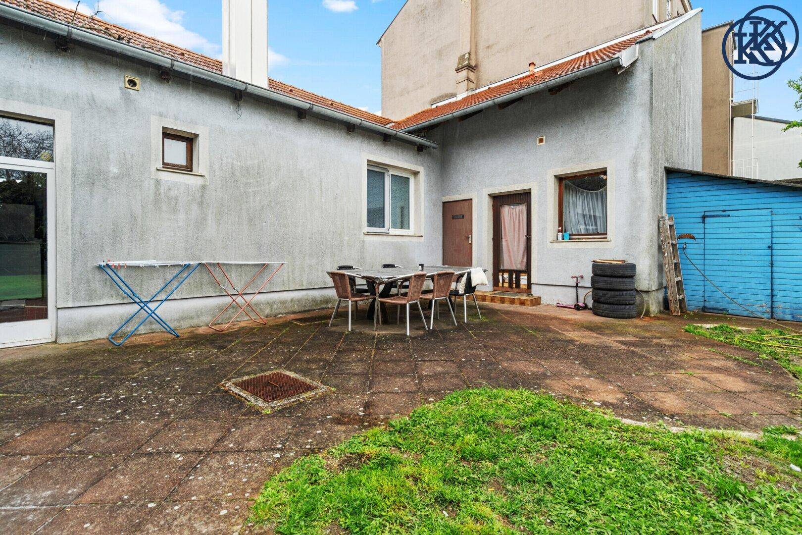 Gepflasterte Terrasse hinter dem Haus mit Sitzgelegenheiten und Zugang zum Garten.