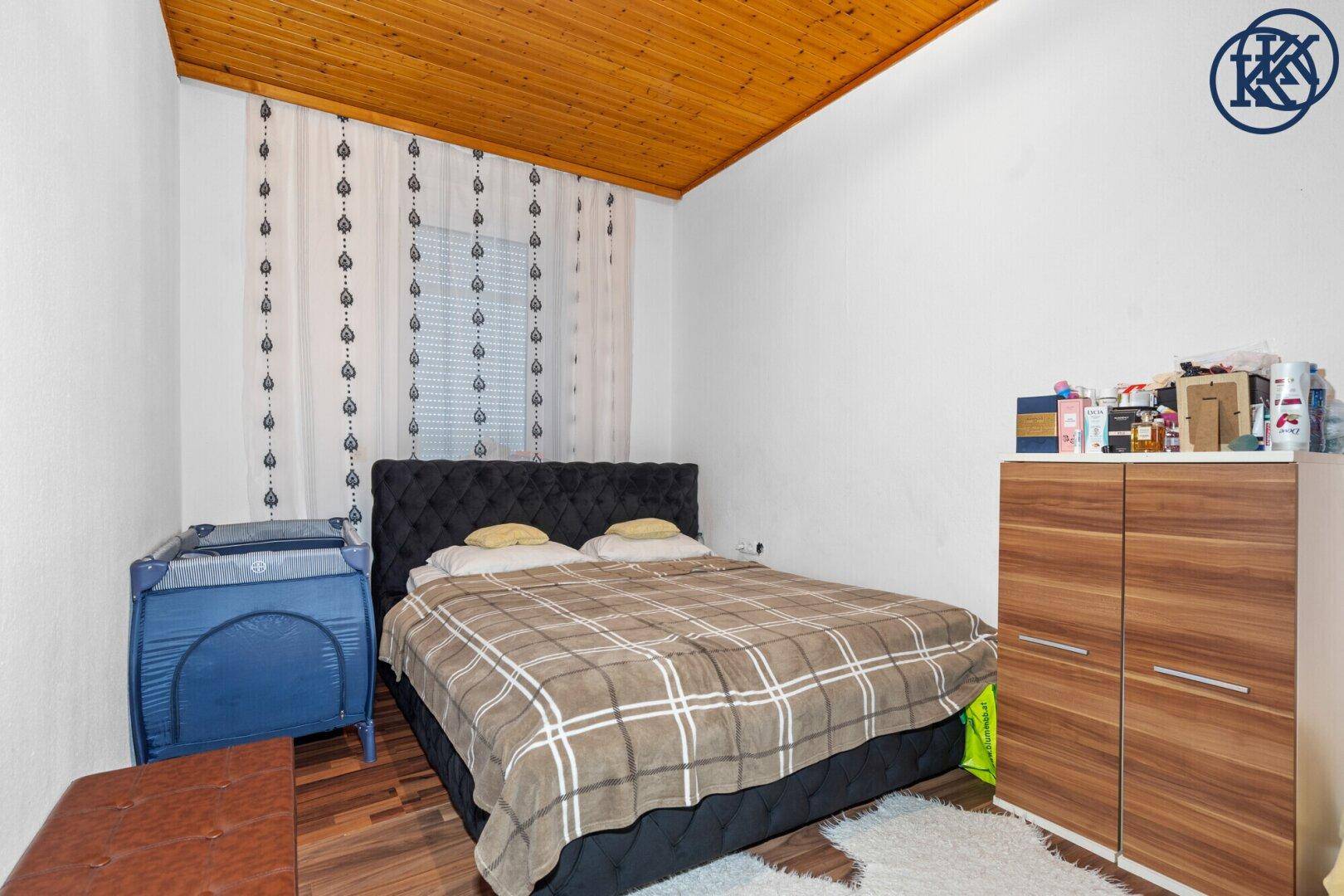 Schlafzimmer mit Doppelbett, Holzdecke und Laminatboden.