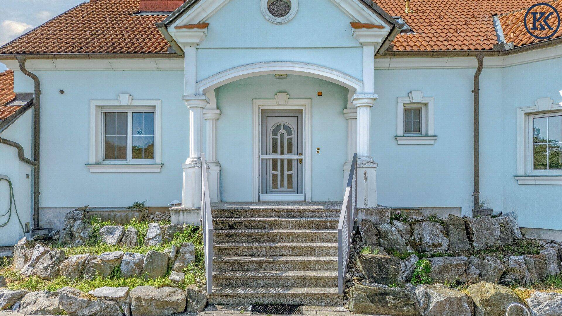 Detailansicht des Haupteingangs mit Säulen, Steintreppe und verzierter Haustür.