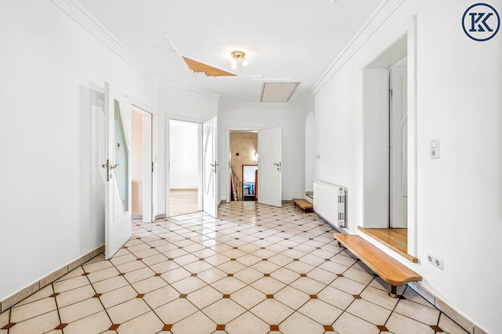 Heller Wohnraum mit Fliesenboden, weißen Wänden und mehreren Türen zu angrenzenden Zimmern.