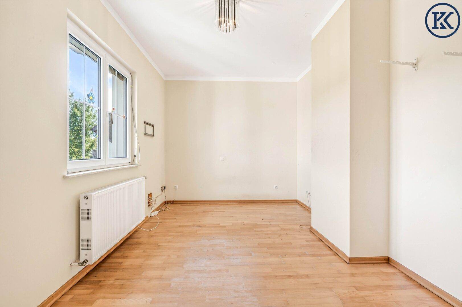Helles Zimmer mit Laminatboden in Holzoptik, beigen Wänden und großem Fenster.