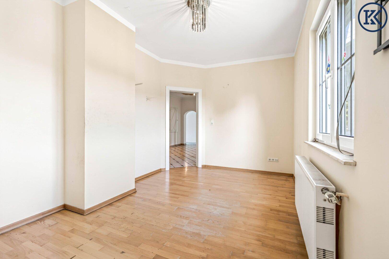 Geräumiges Zimmer mit hellem Laminatboden, beigen Wänden und Zugang zu weiteren Räumen.