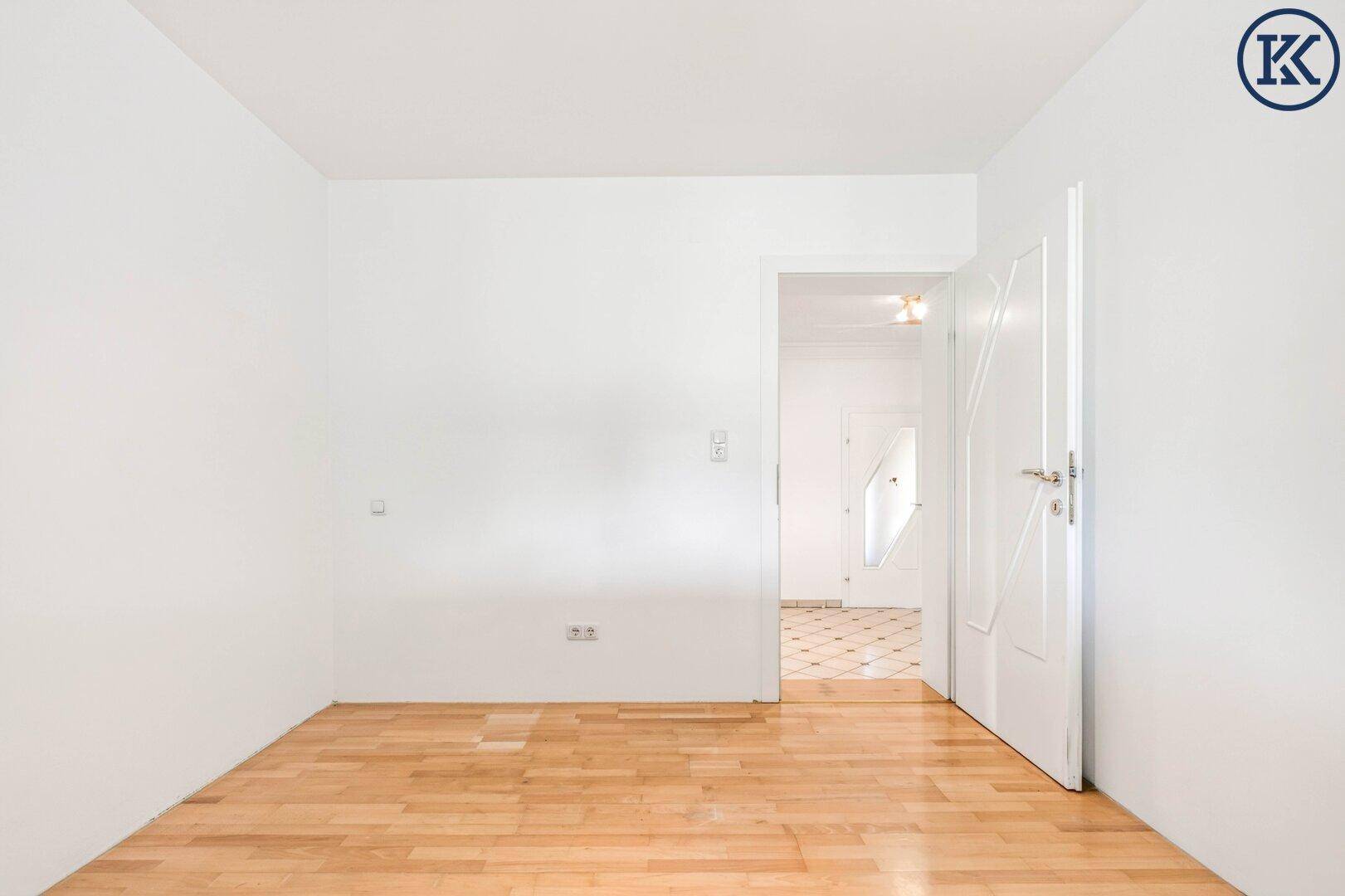 Schlichtes Zimmer mit hellem Laminatboden, weißen Wänden und Zugang zu einem anderen Raum.