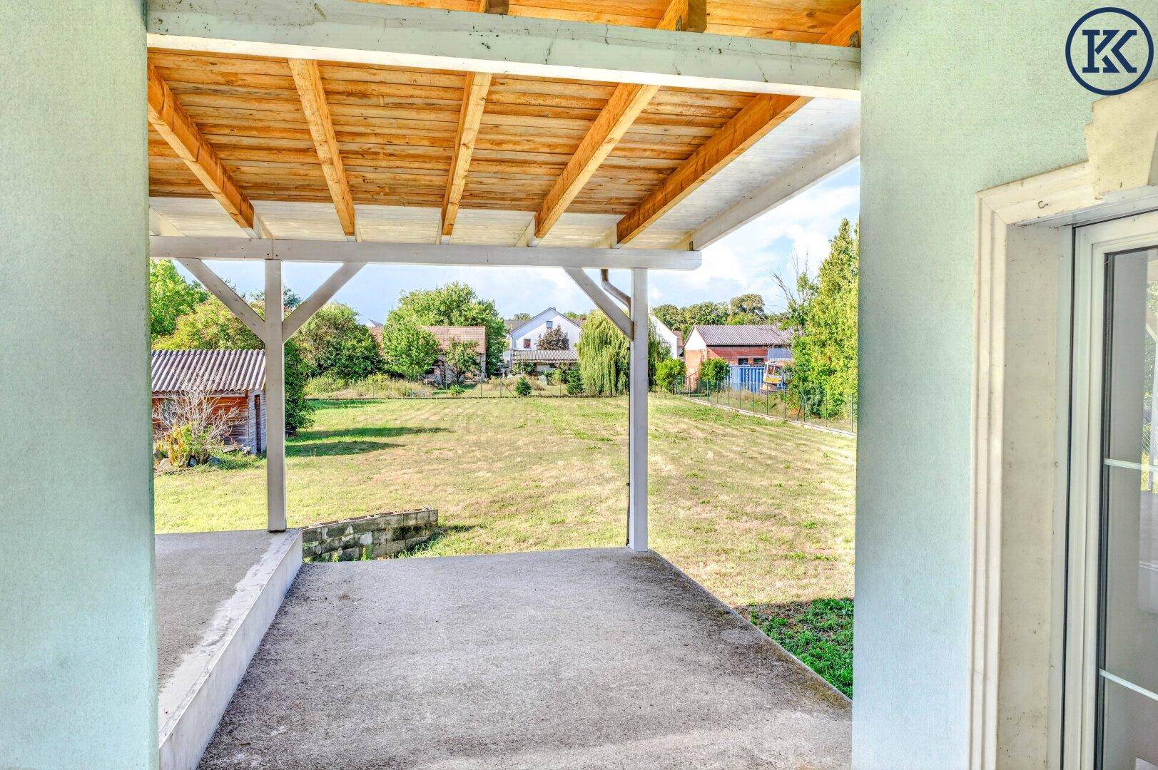 Geräumige überdachte Terrasse mit Holzdach und freiem Blick auf den großen Garten.