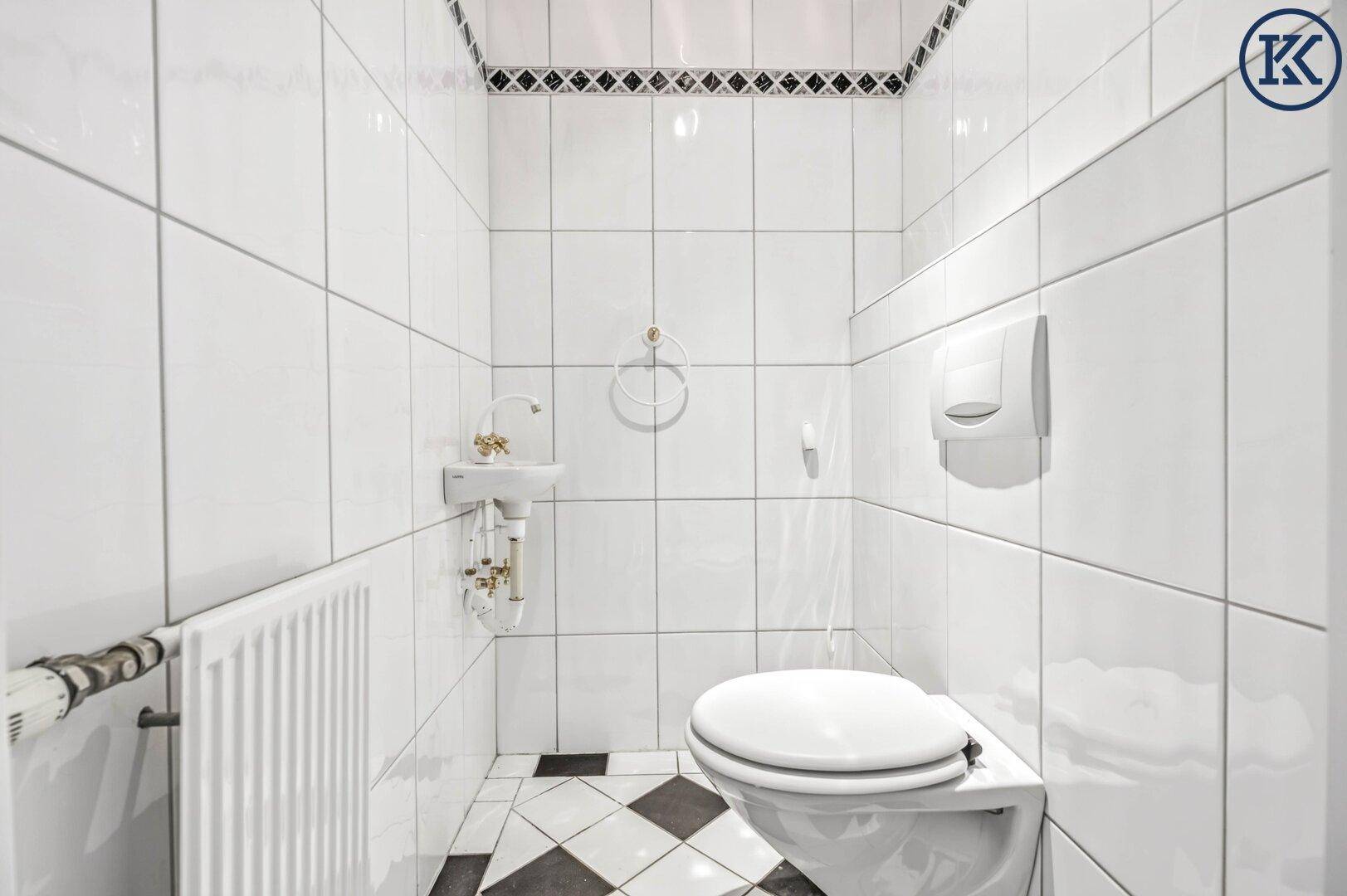 Kleines Gäste-WC mit weißen Fliesen, Wand-WC und einem kleinen Handwaschbecken.