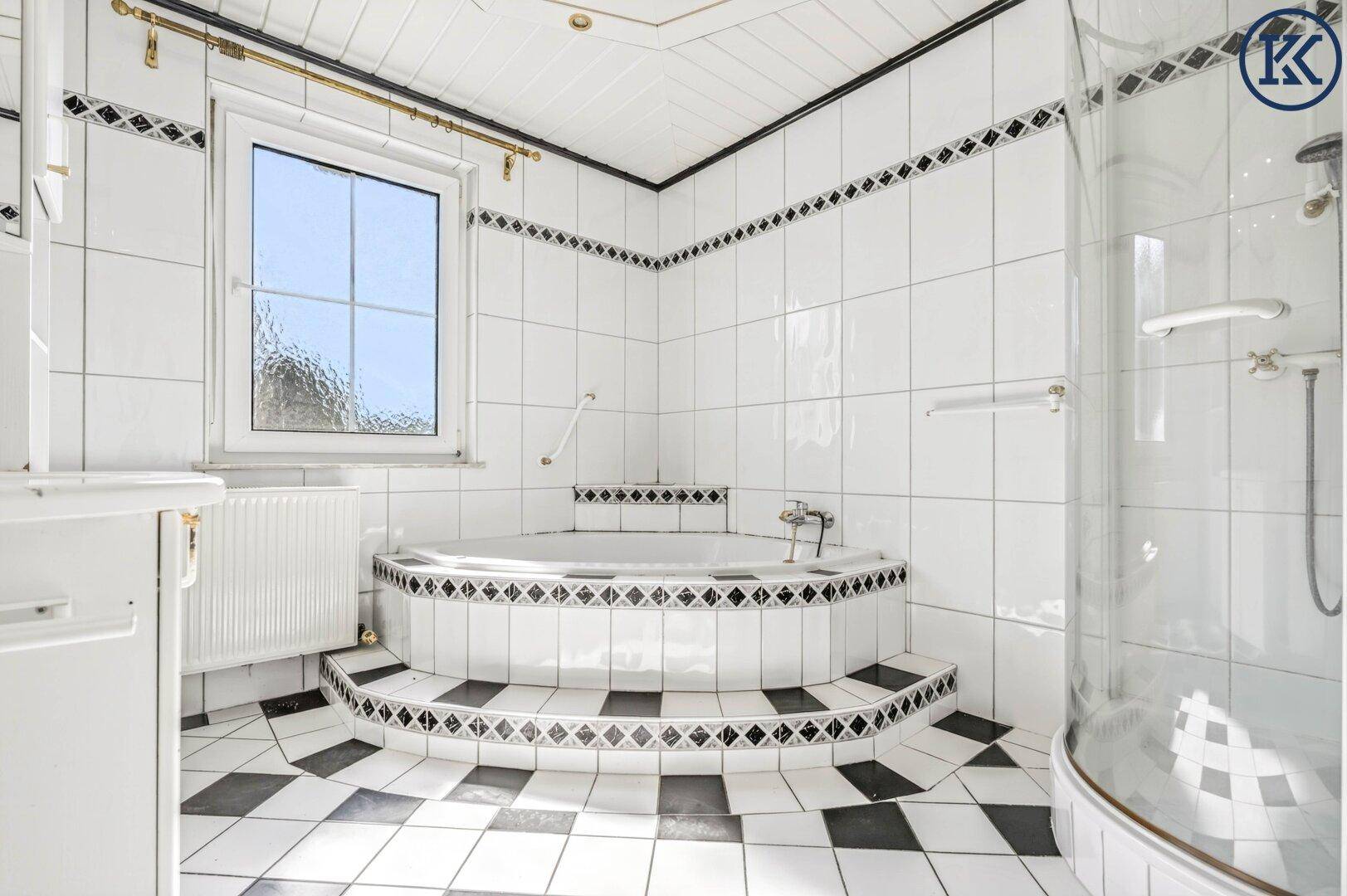 Helles Badezimmer mit markanten schwarz-weißen Fliesen, Eckbadewanne und Fenster.