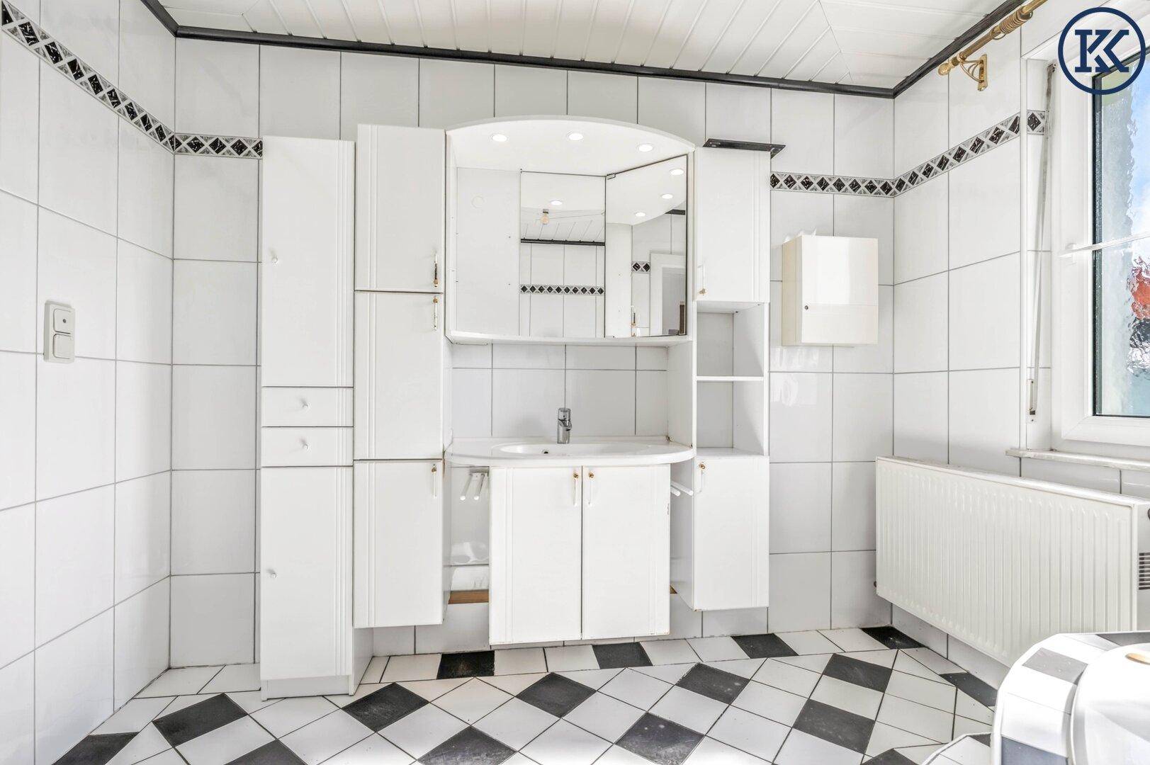 Badezimmer mit weißem Waschtisch, Spiegelschrank und schwarz-weißem Fliesenboden.