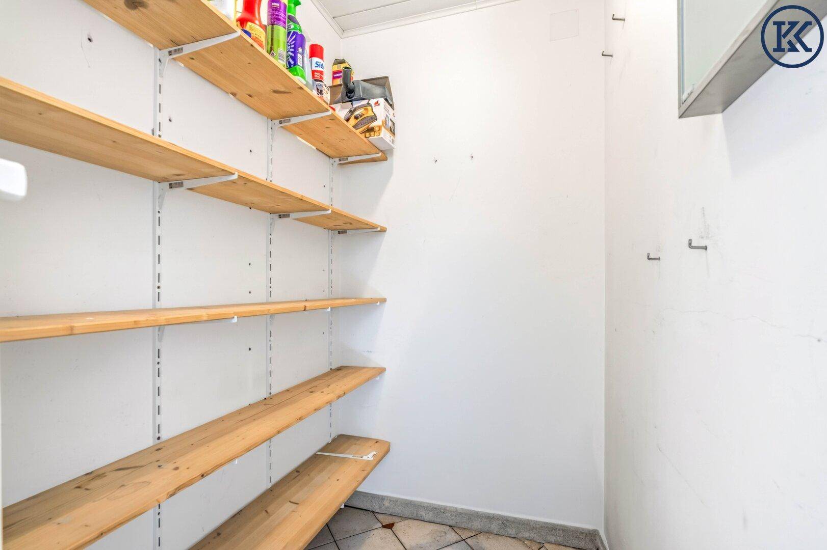 Praktischer Abstellraum mit Holzregalen und gefliestem Boden, ideal für Haushaltsartikel.