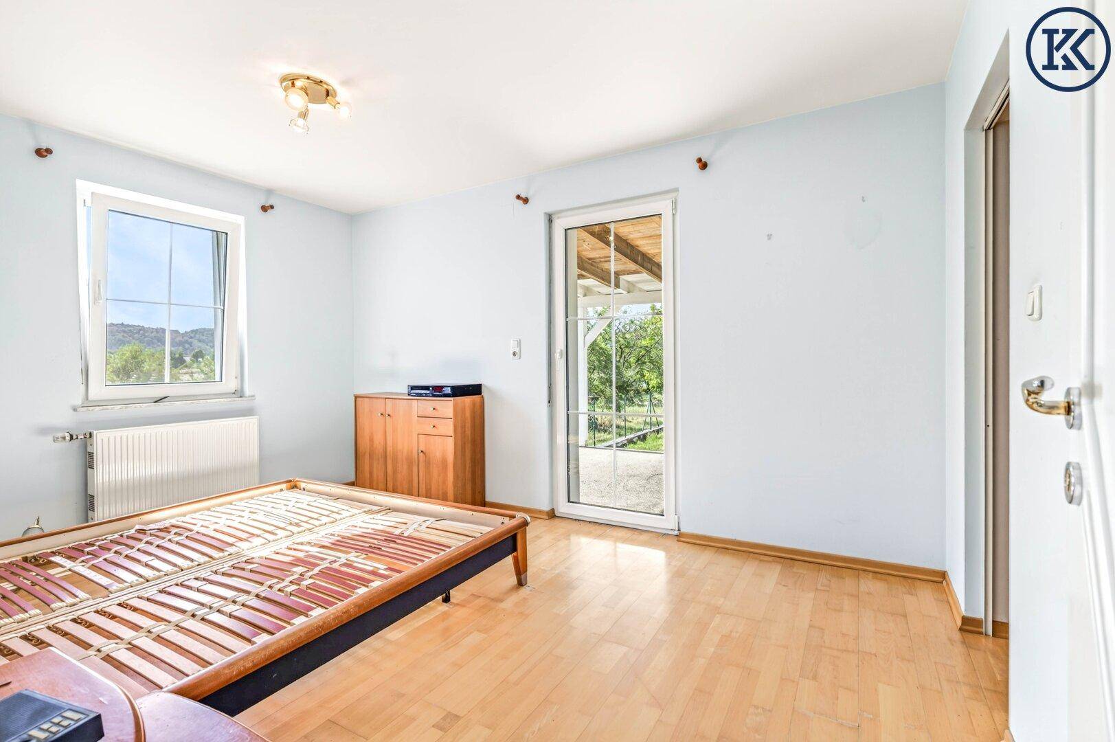 Schlafzimmer mit Holzboden, Fenster und Zugang zu einem Außenbereich, unmöbliert.