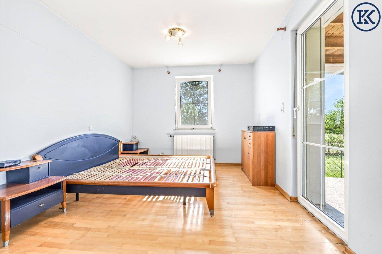 Helles Schlafzimmer mit Holzboden, Fenster und Zugang zu einer Terrasse, mit viel Tageslicht.