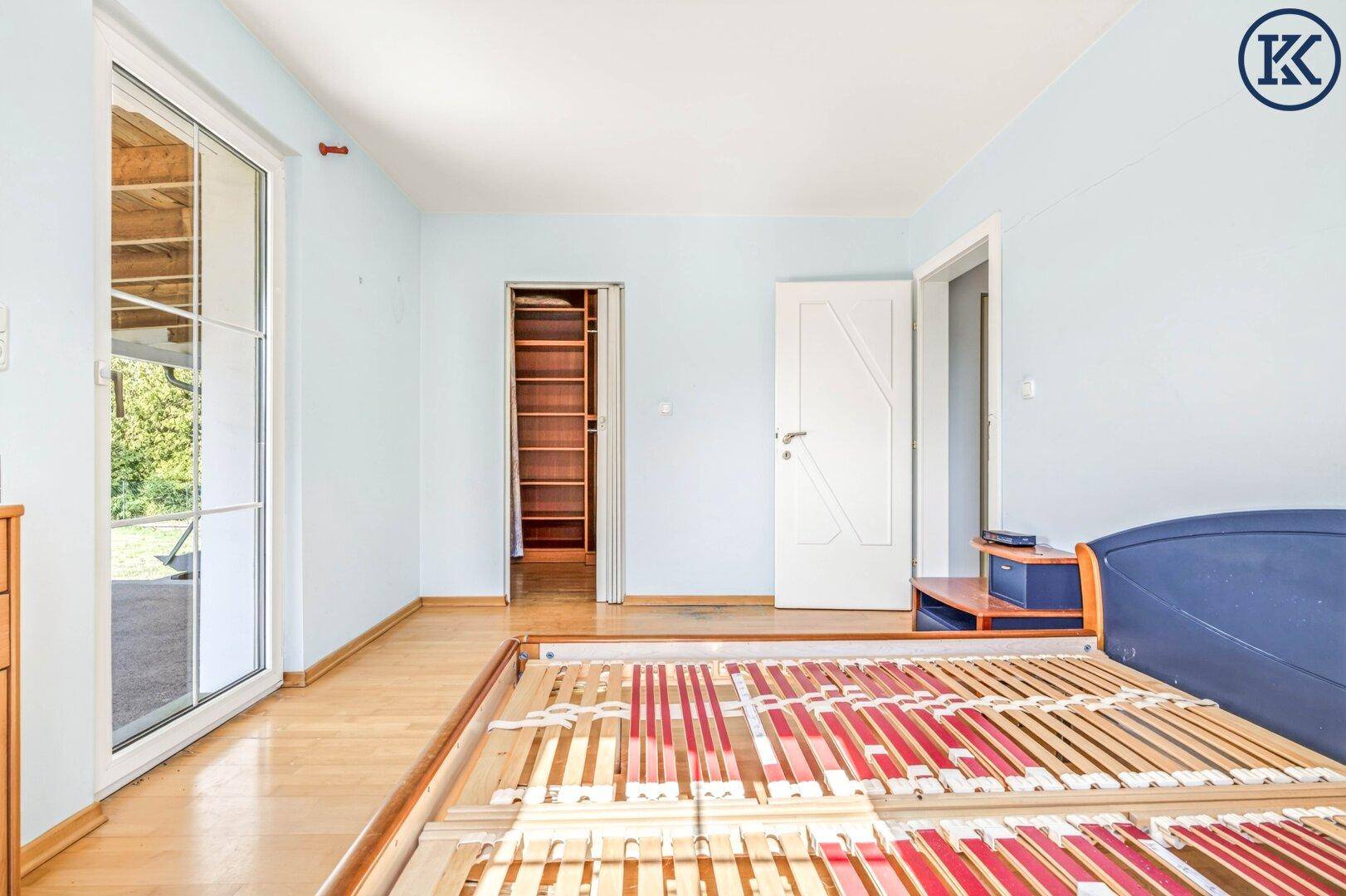Schlafzimmer mit Holzboden, Terrassenzugang und Blick auf einen begehbaren Kleiderschrank.