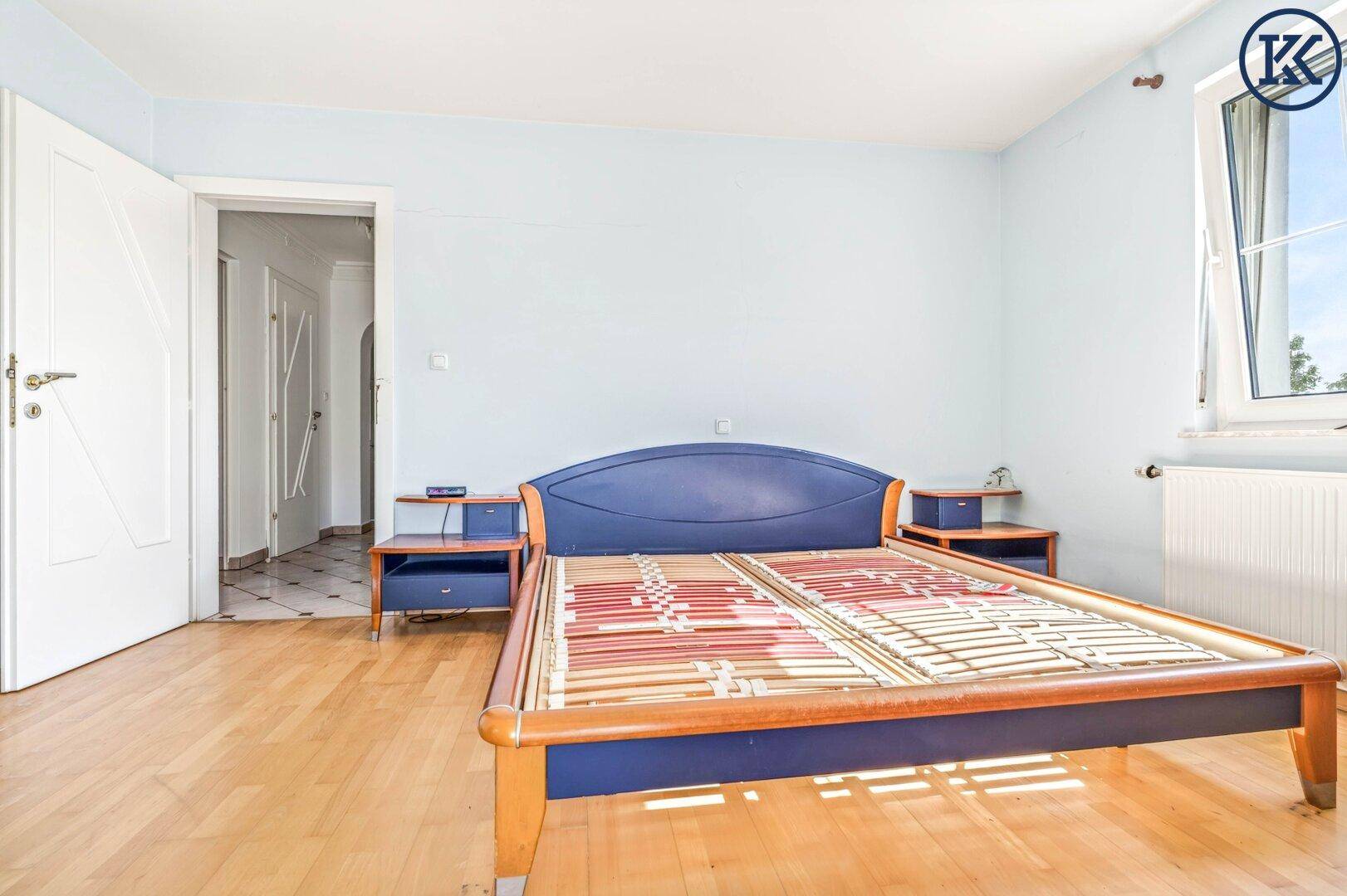 Schlafzimmer mit Holzboden, Fenster und einem Bettgestell, das auf den Flur blickt.