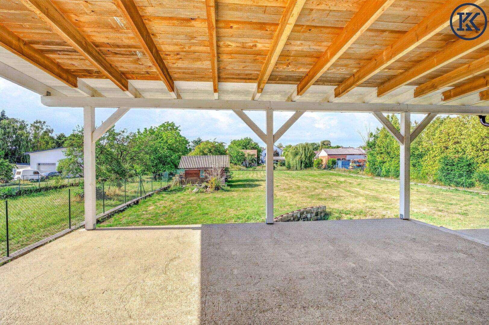 Überdachte Terrasse mit Holzdach und weitem Blick auf den grünen Garten und die umliegende Landschaft.