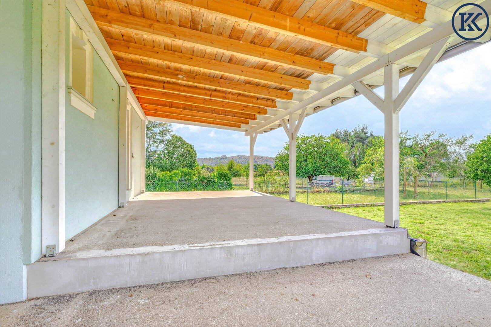 Geräumige überdachte Terrasse mit Holzdach und Stufen, die zum weitläufigen grünen Garten führen.