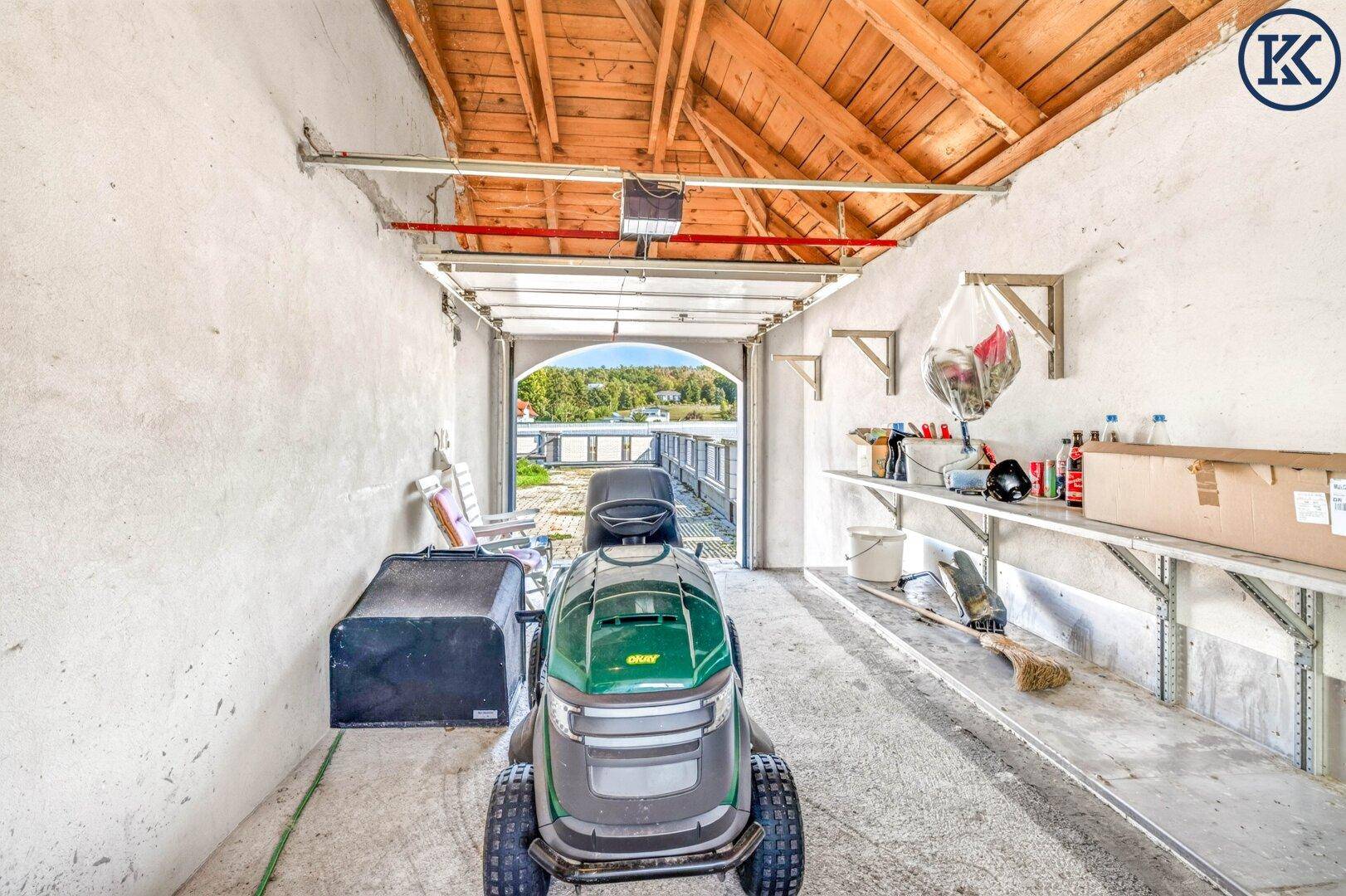 Geräumige Garage oder Werkstatt mit Rasenmäher und Blick auf den See durch das offene Tor.
