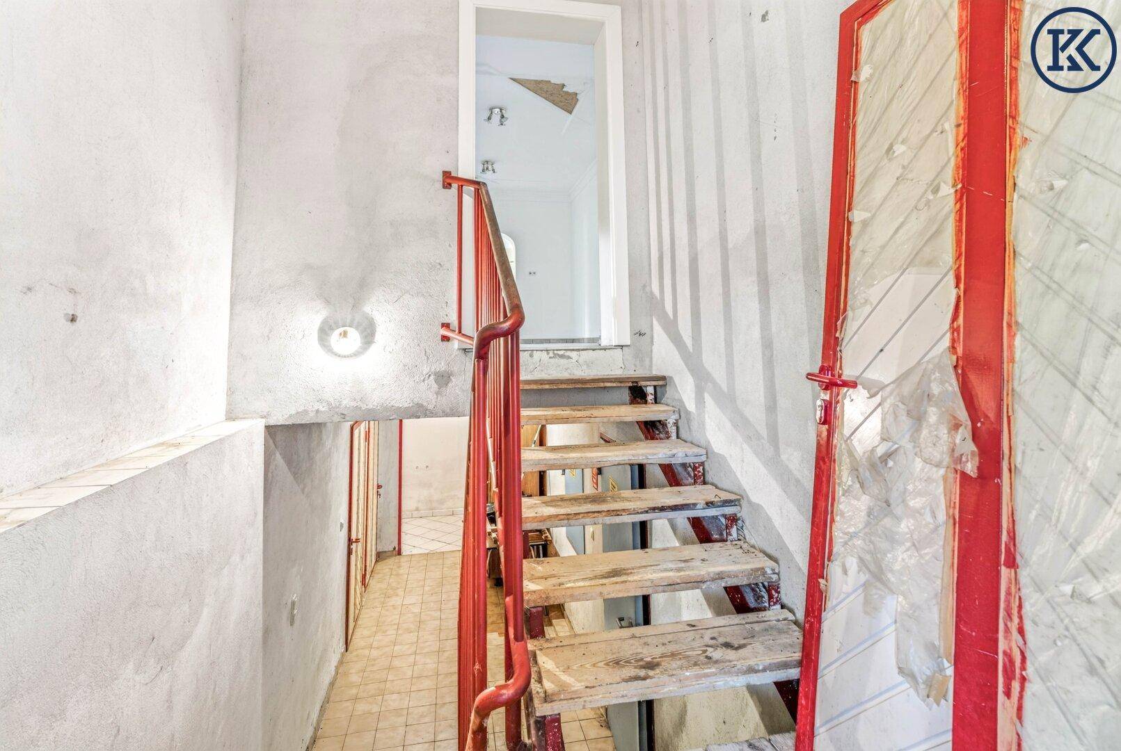 Treppenabgang in den Kellerbereich mit rotem Geländer und unverputzten Wänden.