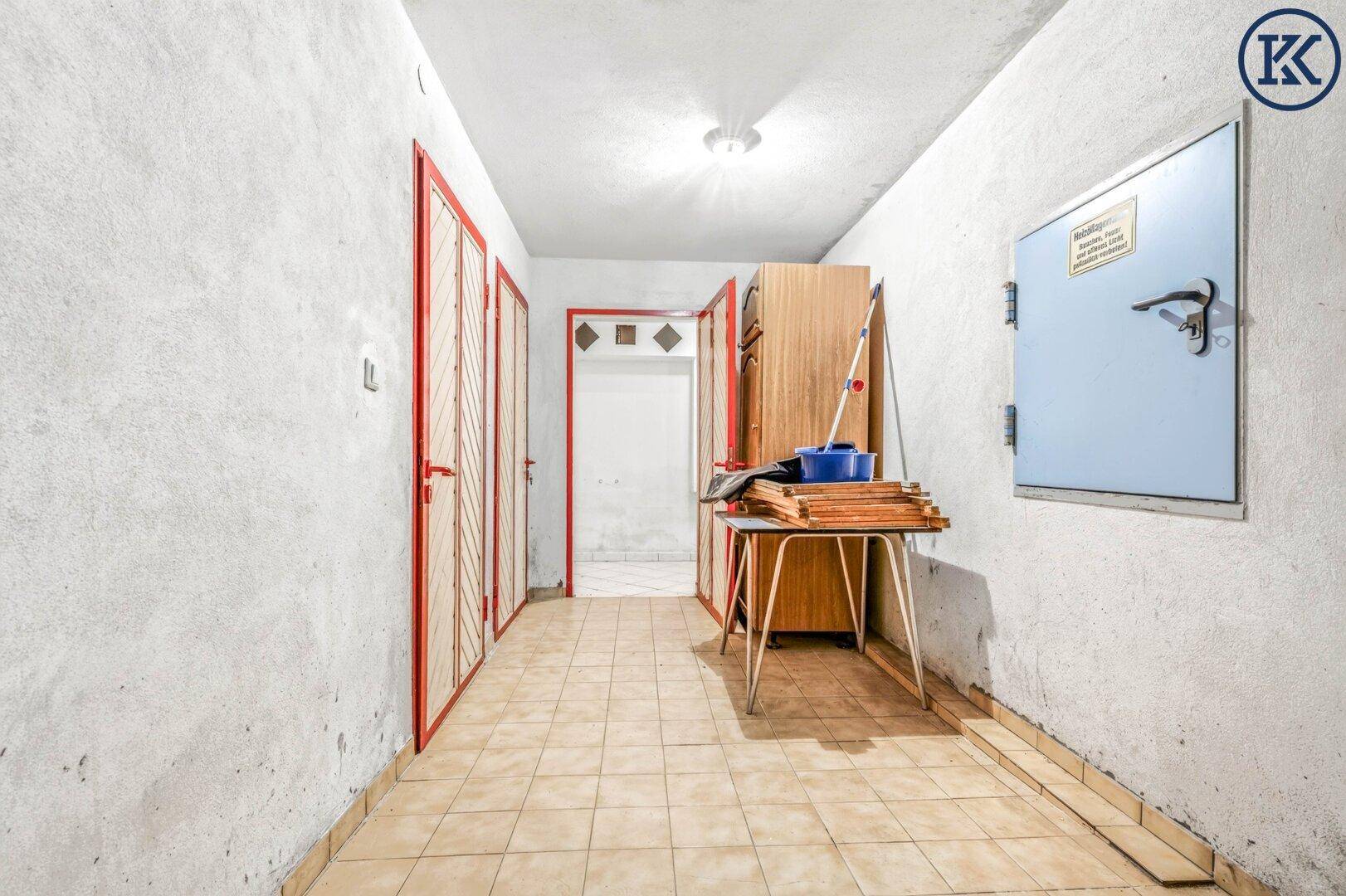 Kellerflur mit Fliesenboden, mehreren Türen und einfachem Stauraum.