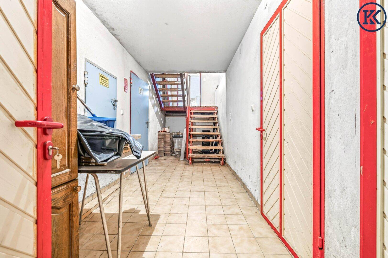 Langer Kellerflur mit Fliesenboden und Zugang zu verschiedenen Räumen sowie zur Treppe.