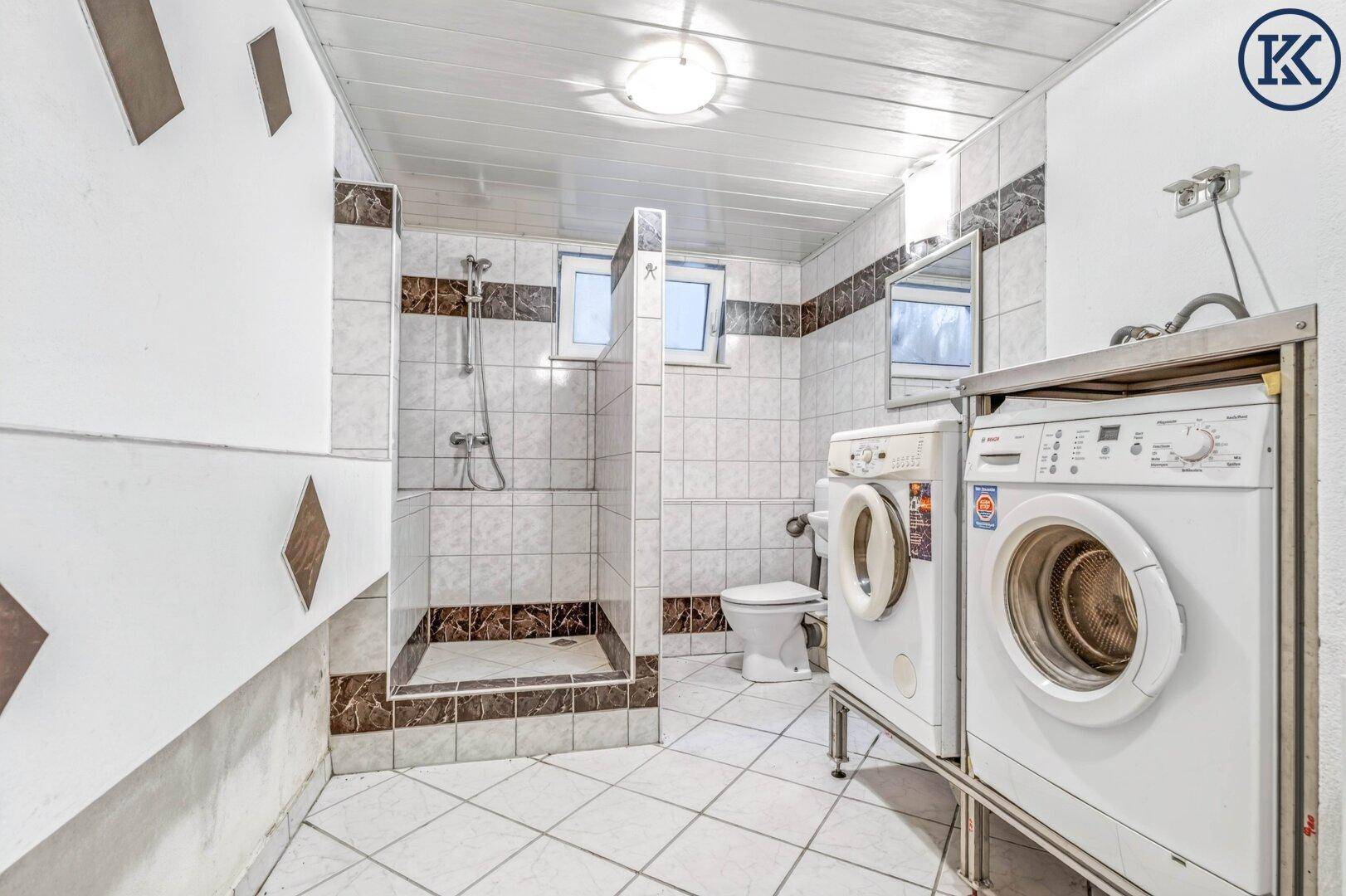 Detailansicht des Kellerbades mit Duschbereich, Toilette und zwei Waschmaschinen.