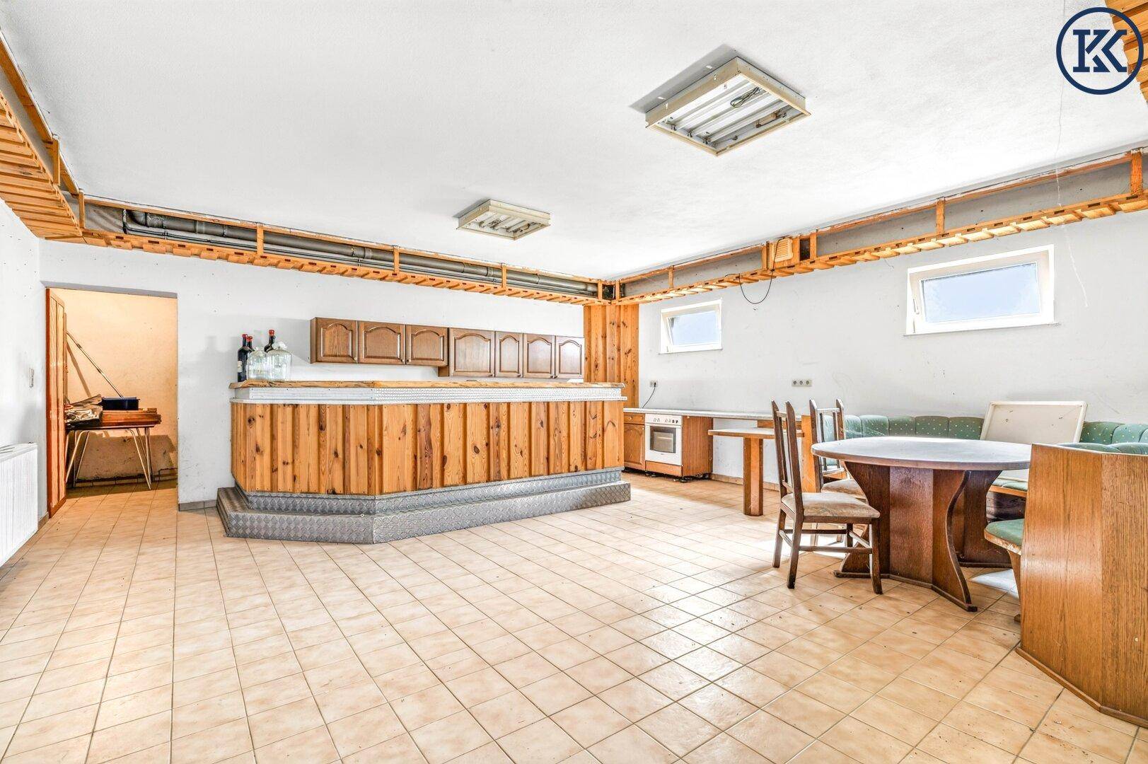 Großer Kellerraum mit Holzbar, Essbereich und Fliesenboden, ideal für gesellige Anlässe.