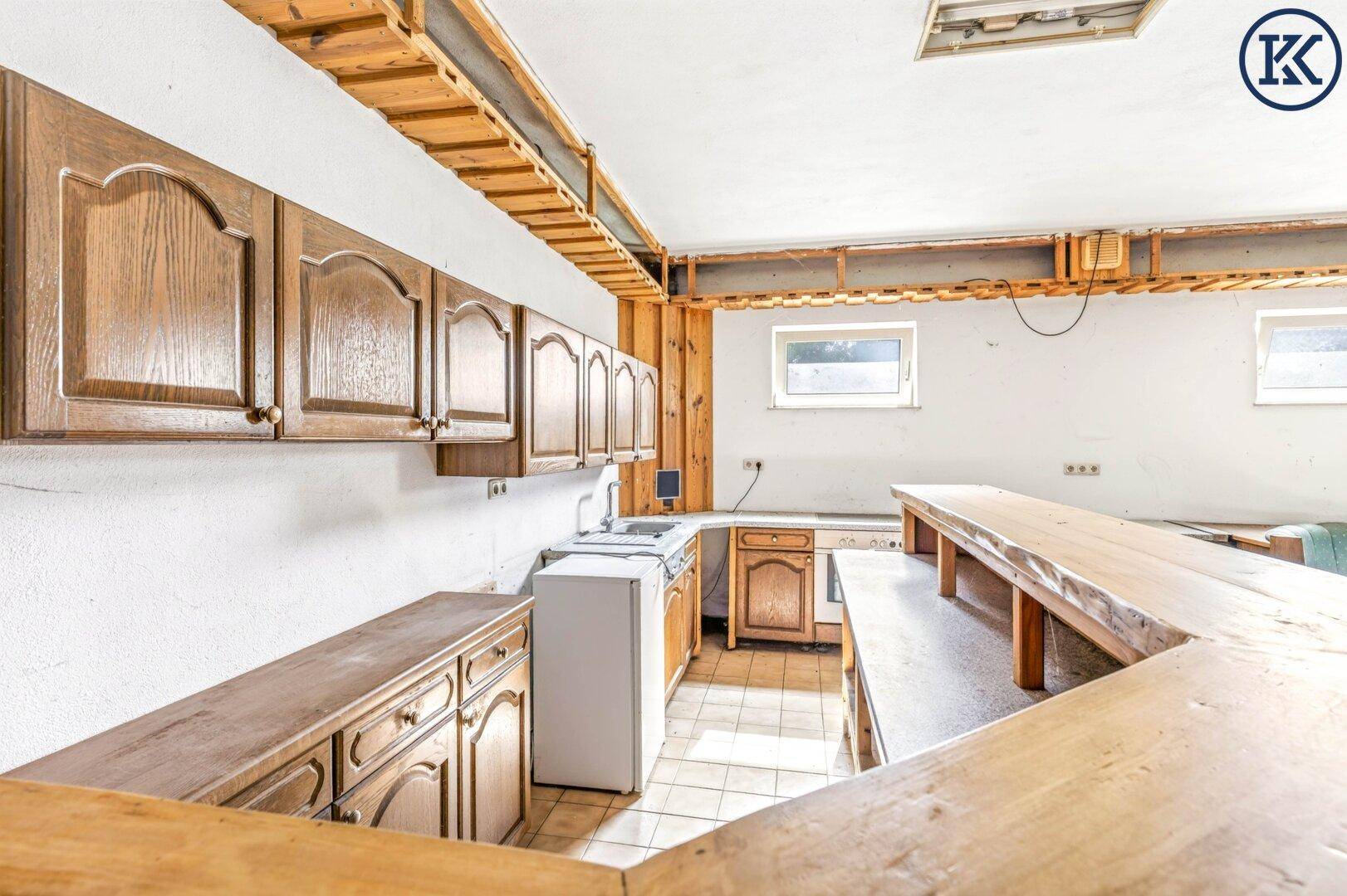 Küchenzeile im Kellerraum mit Holzschränken, Spüle und kleinem Kühlschrank.