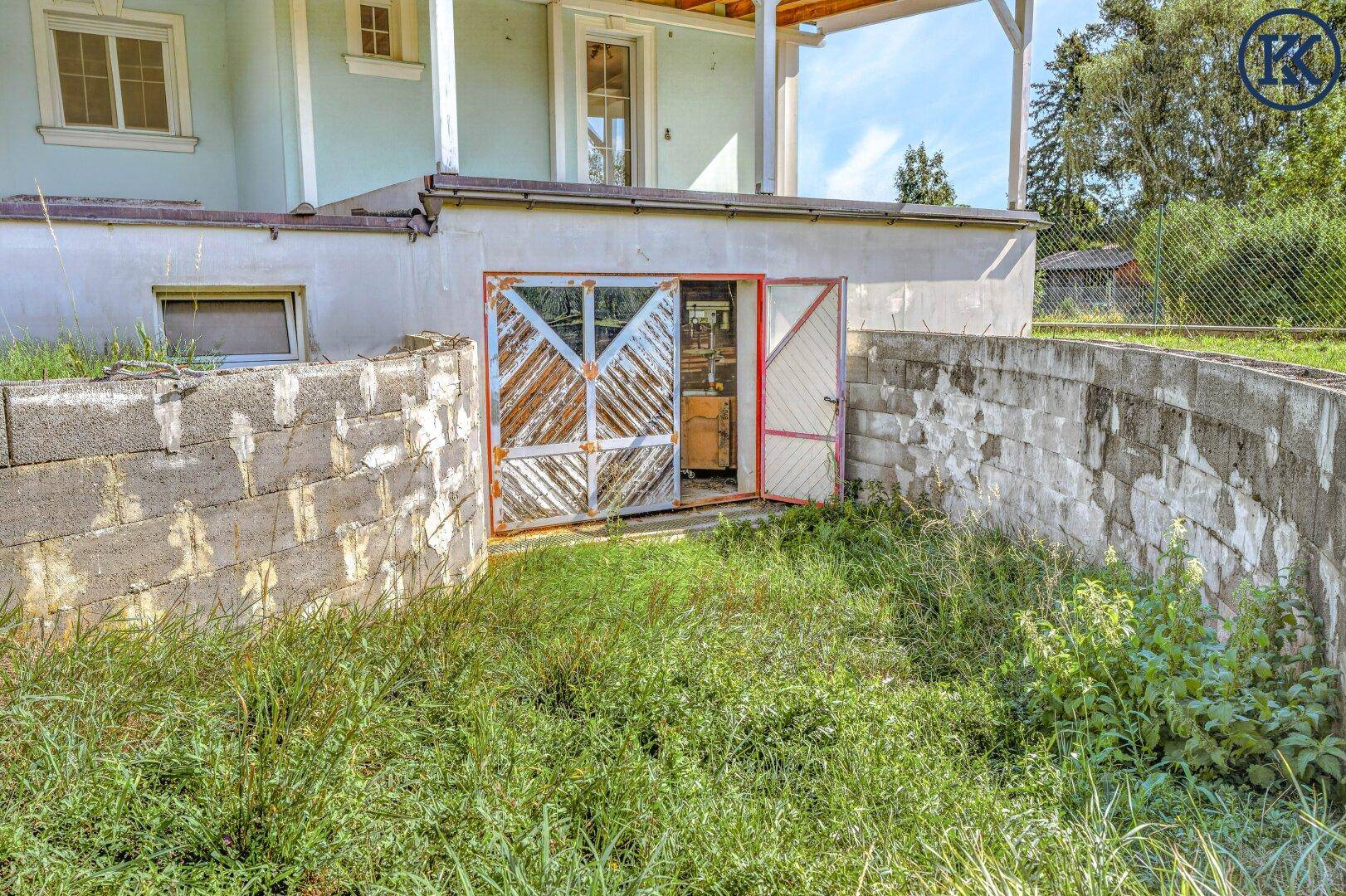 Eingang zum Keller oder zur Garage mit rustikalen Holztüren, umgeben von Betonmauern und Gras.