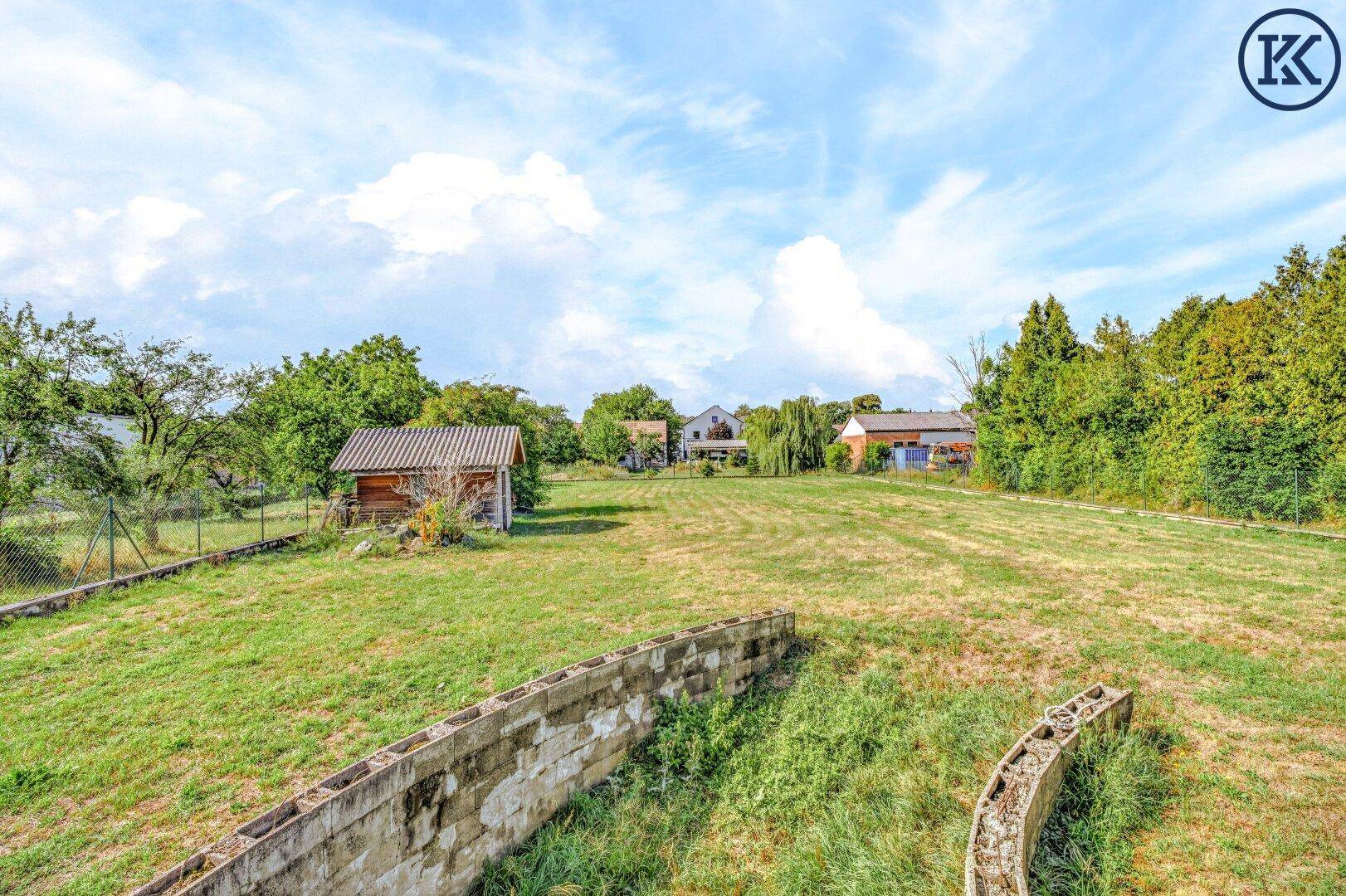 Weitläufiges Gartengrundstück mit Rasenfläche, einem kleinen Holzschuppen und Bäumen im Hintergrund der Landschaft.