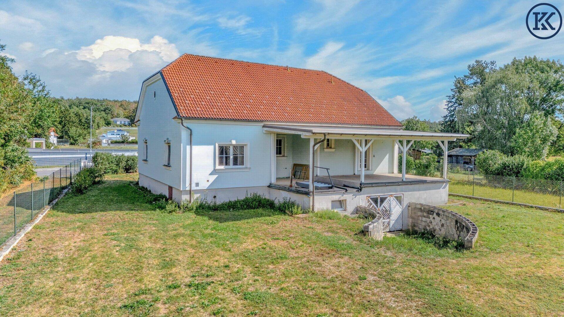 Hausansicht von der Seite mit überdachter Veranda und Zugang zum Kellerbereich, umgeben von Rasen.