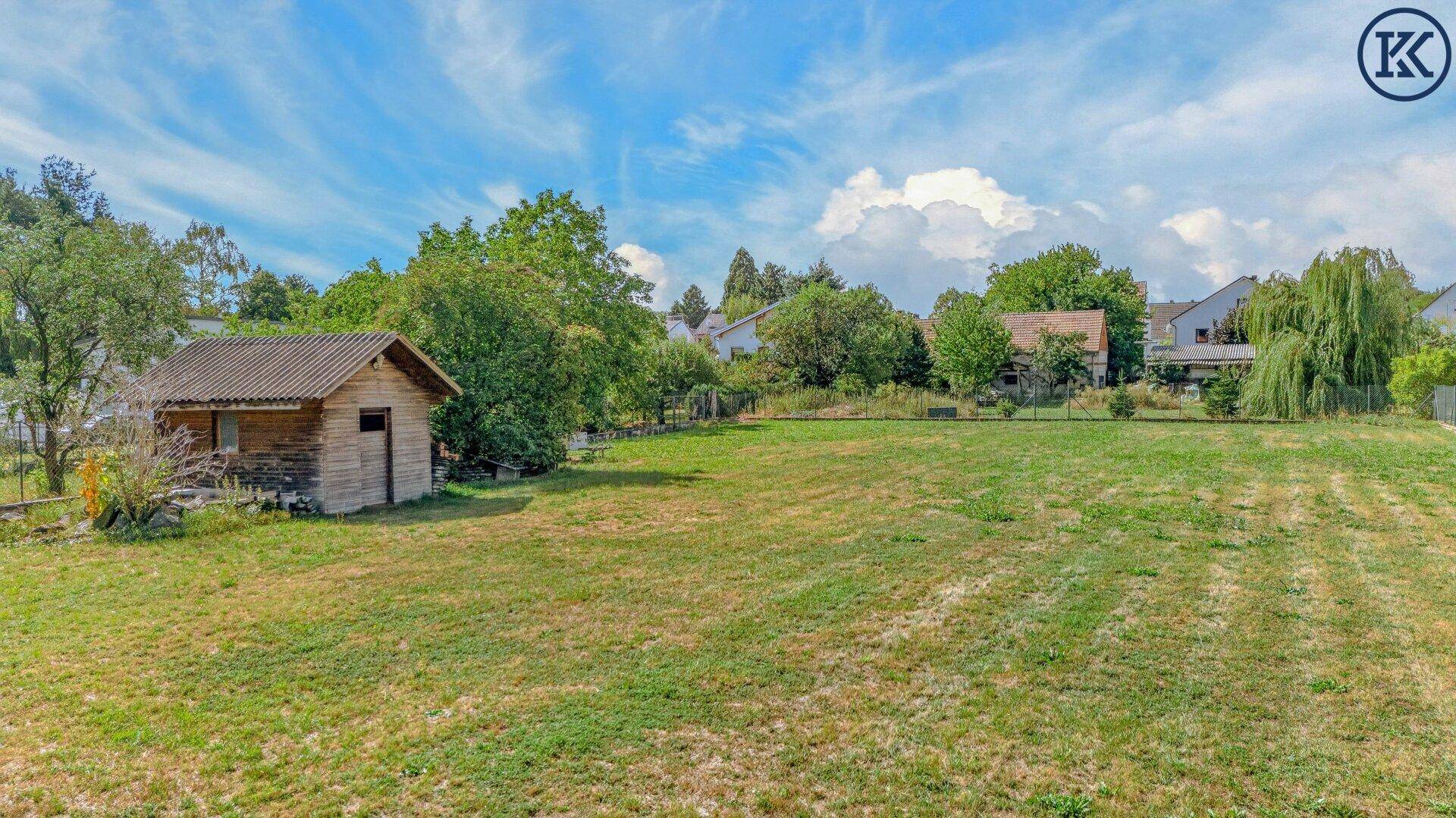 Großes Gartengrundstück mit Rasenfläche, einem Holzschuppen und umgebender Natur unter weitem Himmel.